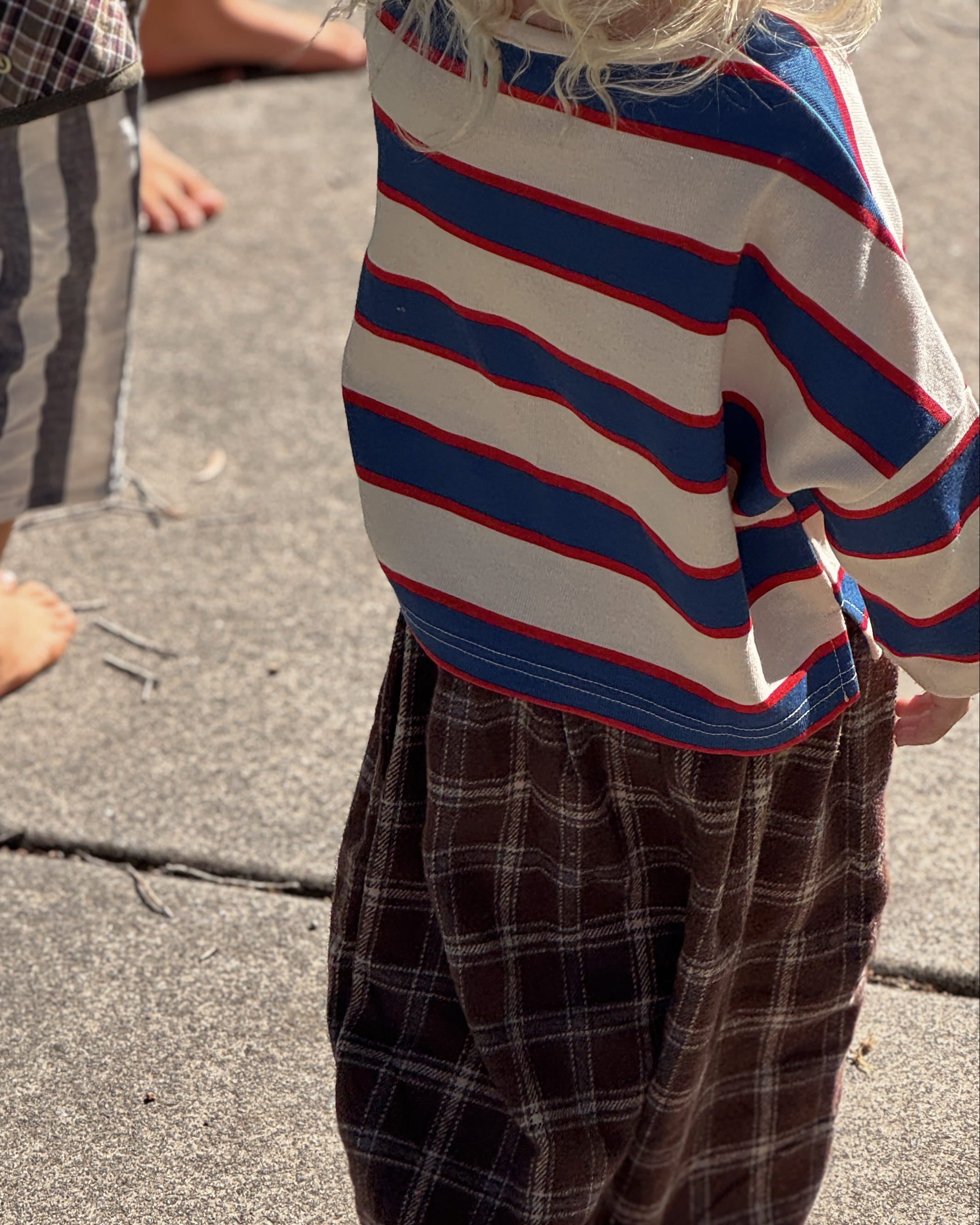 Two children standing on a concrete surface, one wearing a striped sweater and plaid pants.