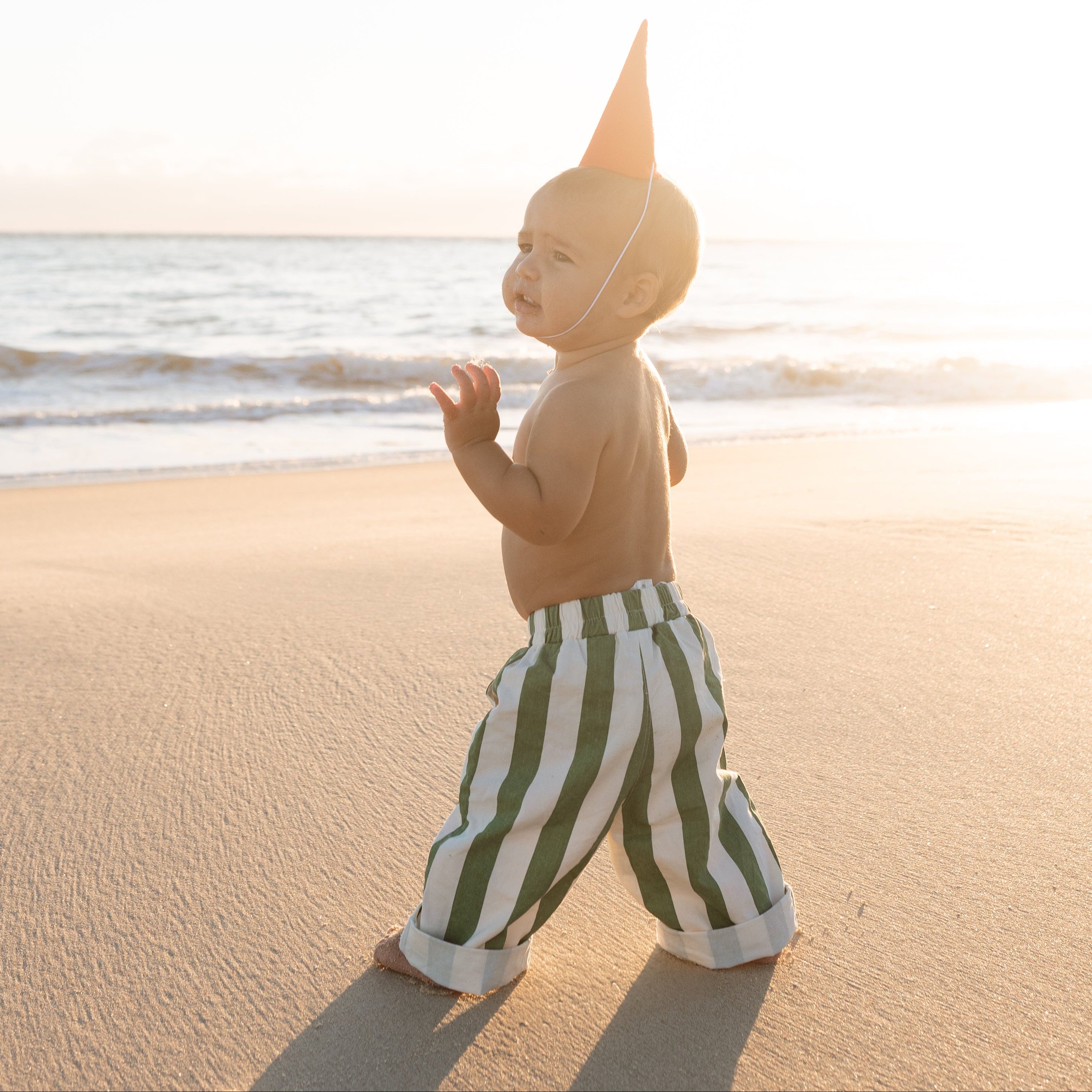 infant beach wear baby and toddler boys green and white striped pants walking on the beach 