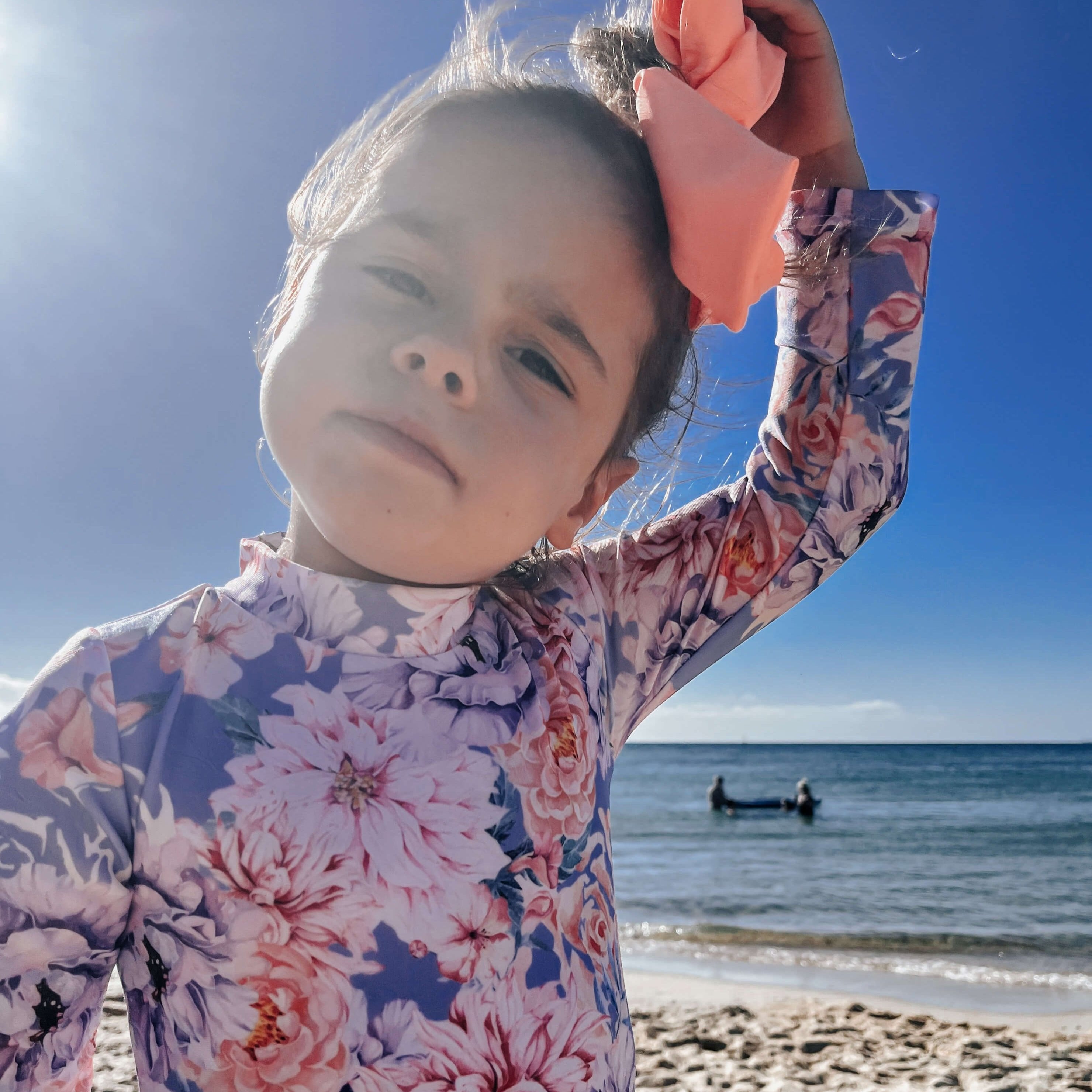 Toddler wearing the best long sleeve sun safe swimsuit with nappy change snaps in a blue and floral color