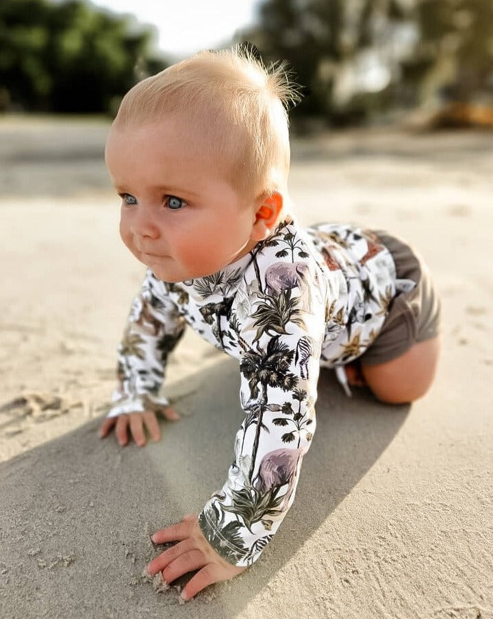 baby boy wearing a rashguard with rear zip and swim shorts with jungle animals all over them.