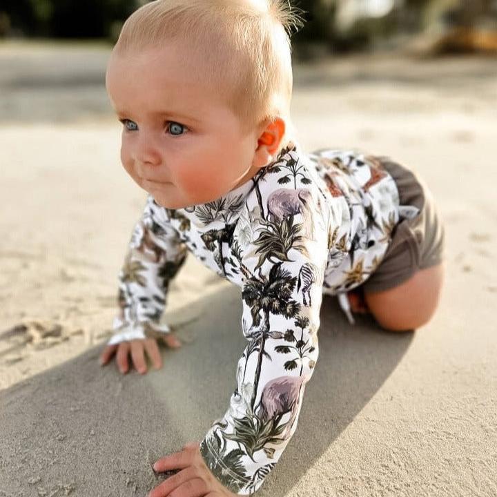 baby boy wearing a rashguard with rear zip and swim shorts with jungle animals all over them. Boys swimwear