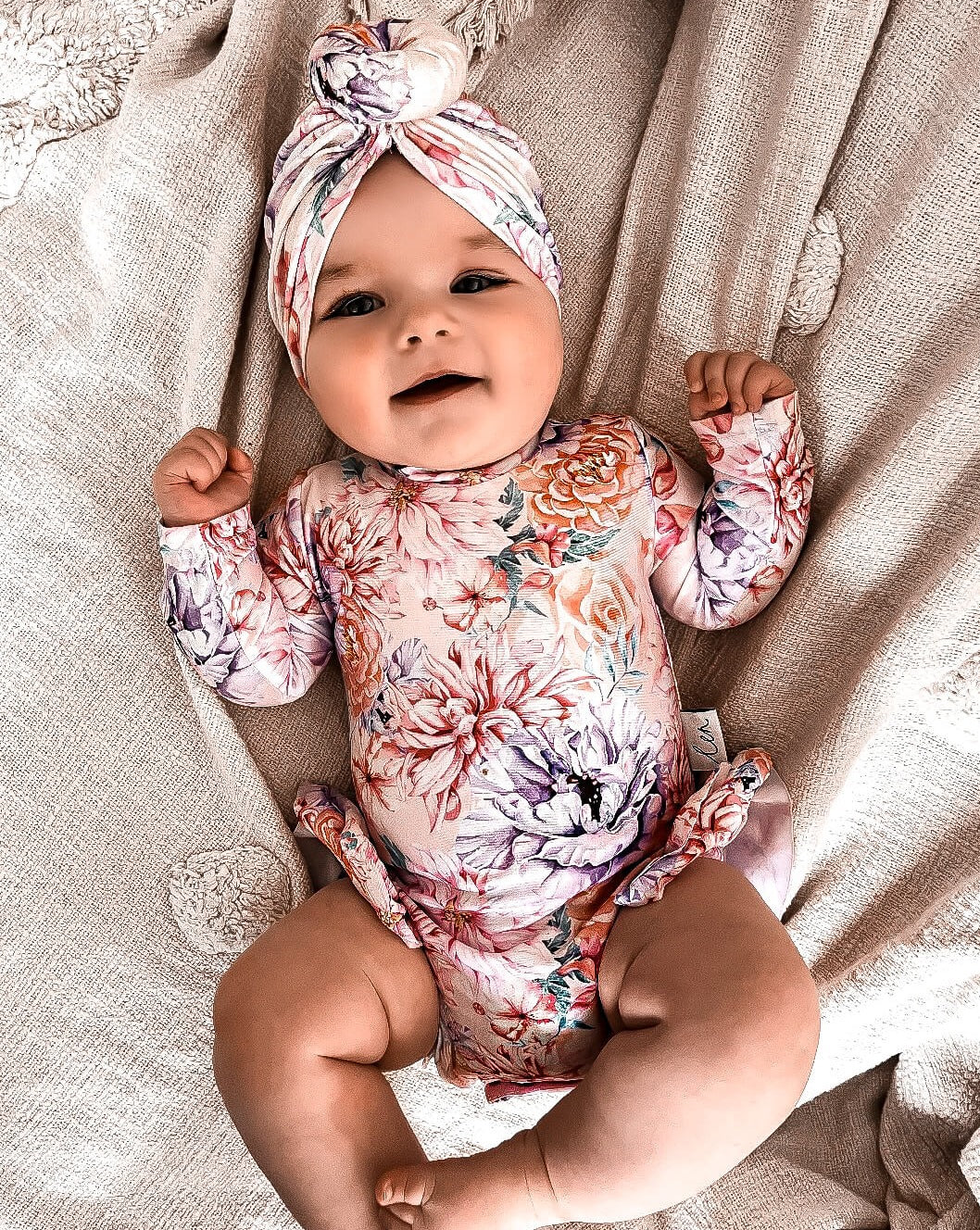 Cute baby girl wearing a floral nappy change swimsuit that has snaps for easy access to nappy changes. The baby girl is wearing a matching swim turban.