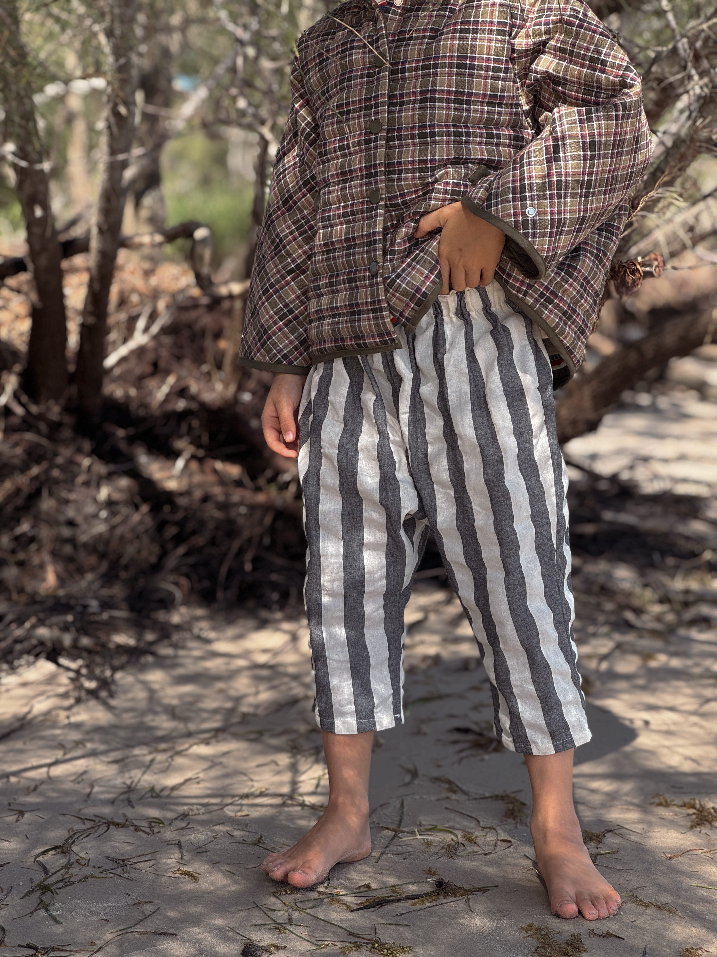 Person wearing a plaid shirt and striped pants standing outdoors on a stone path.