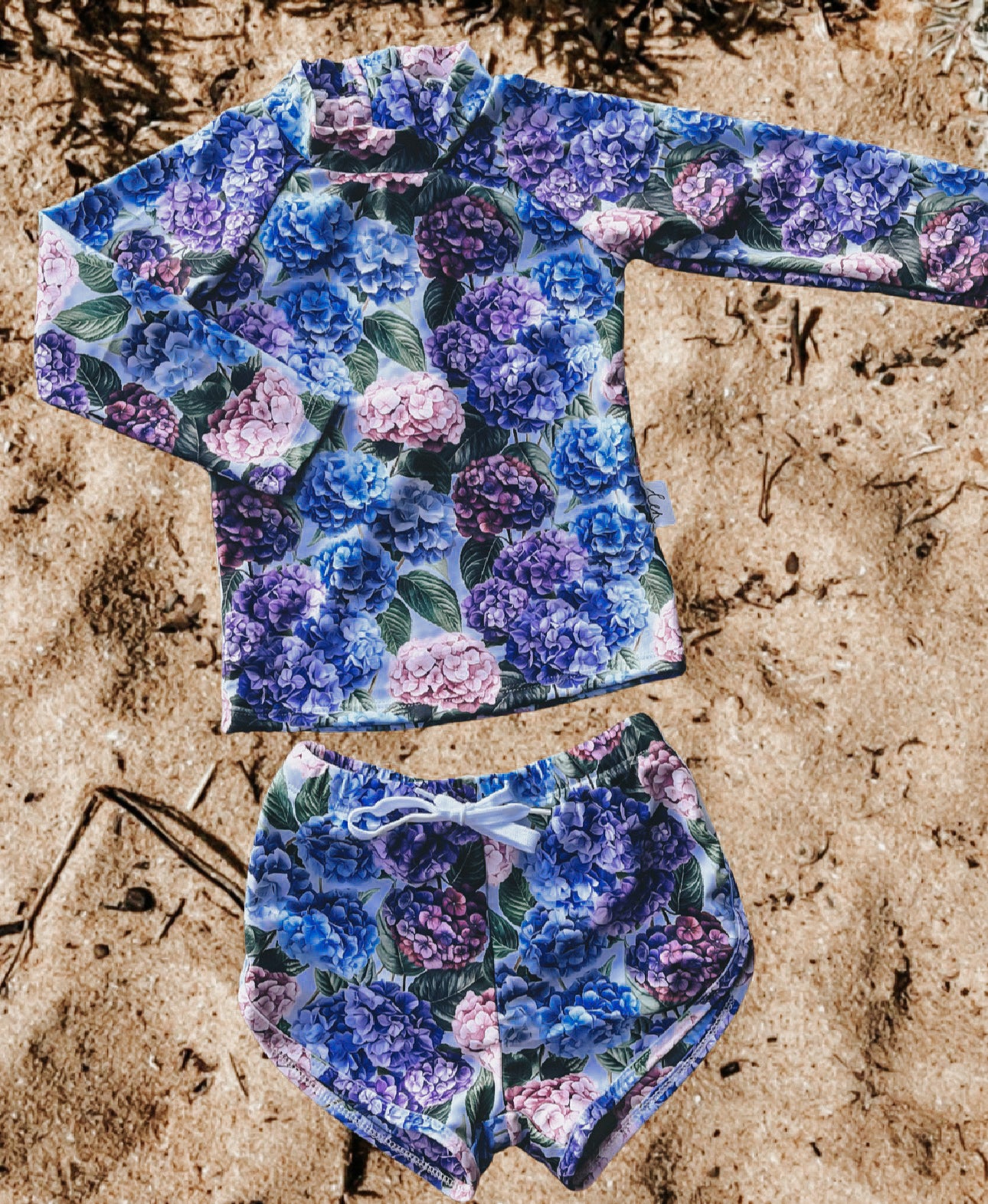 Floral patterned long-sleeve girls rash swim top and shorts set on sandy surface