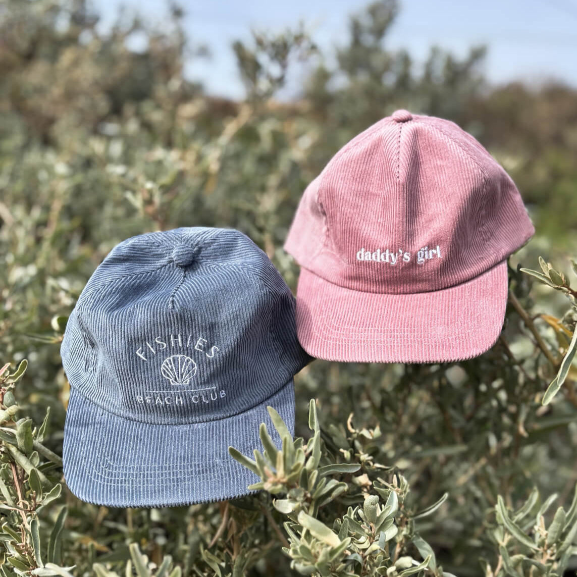 Two kids caps, one blue and one pink, on a bush with a blurred natural background