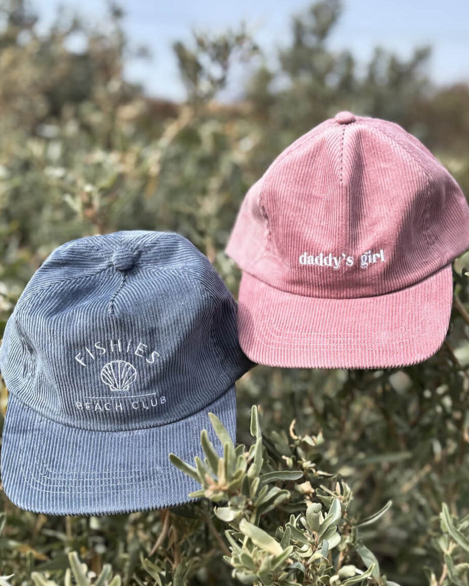 Two kids caps, one blue and one pink, on a bush with a blurred natural background