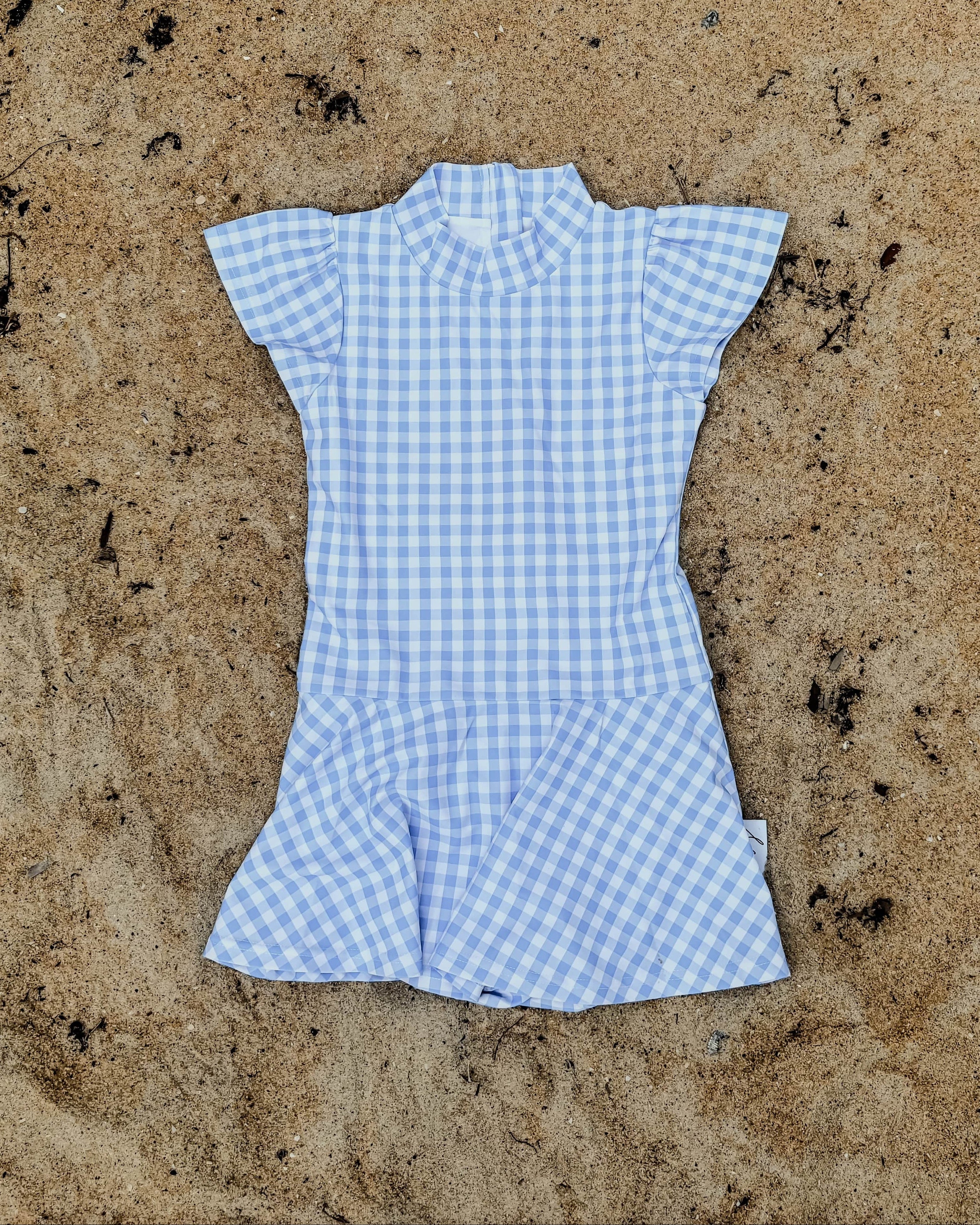 Blue checkered swim dress on sandy ground with seaweed