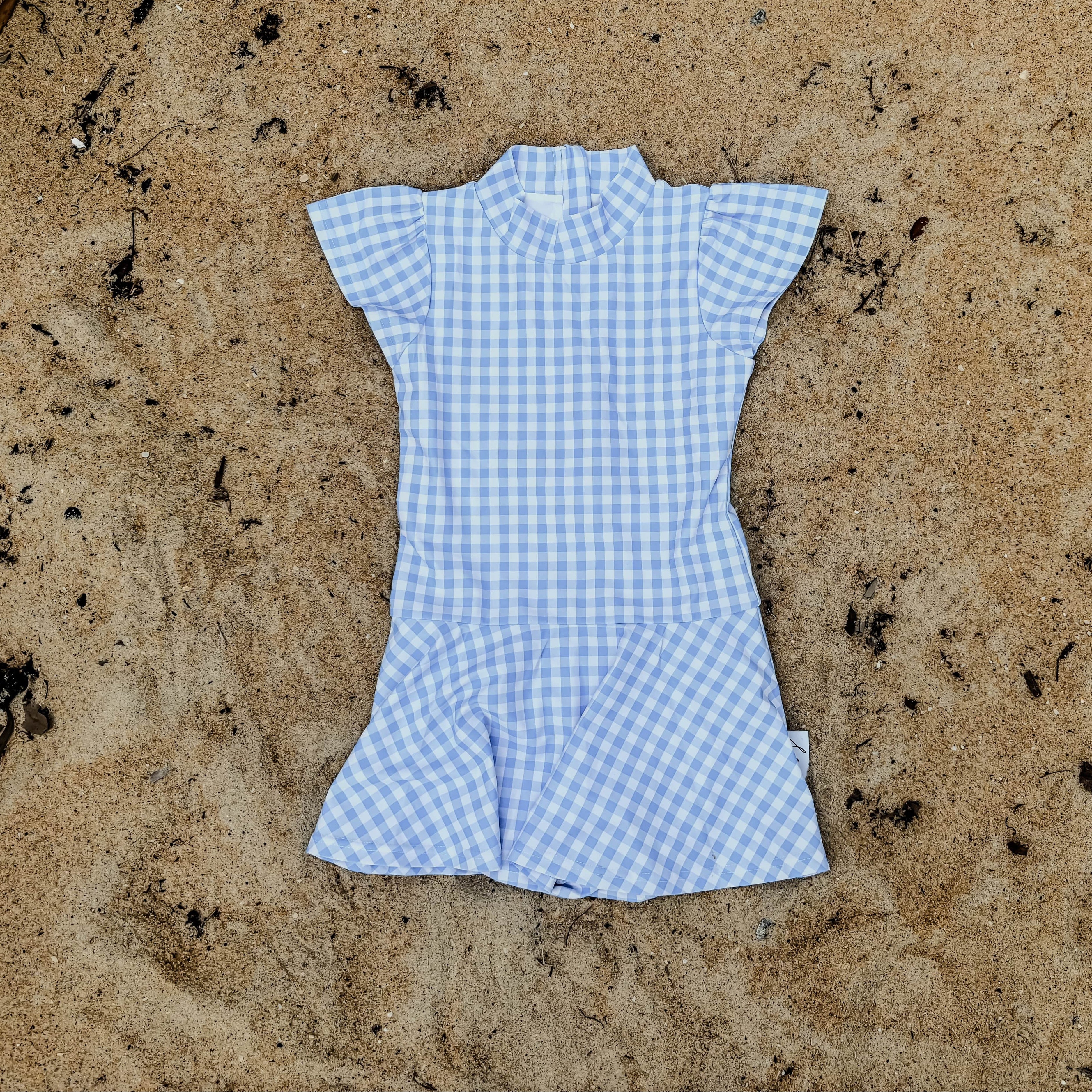 Blue checkered swim dress on sandy ground with seaweed