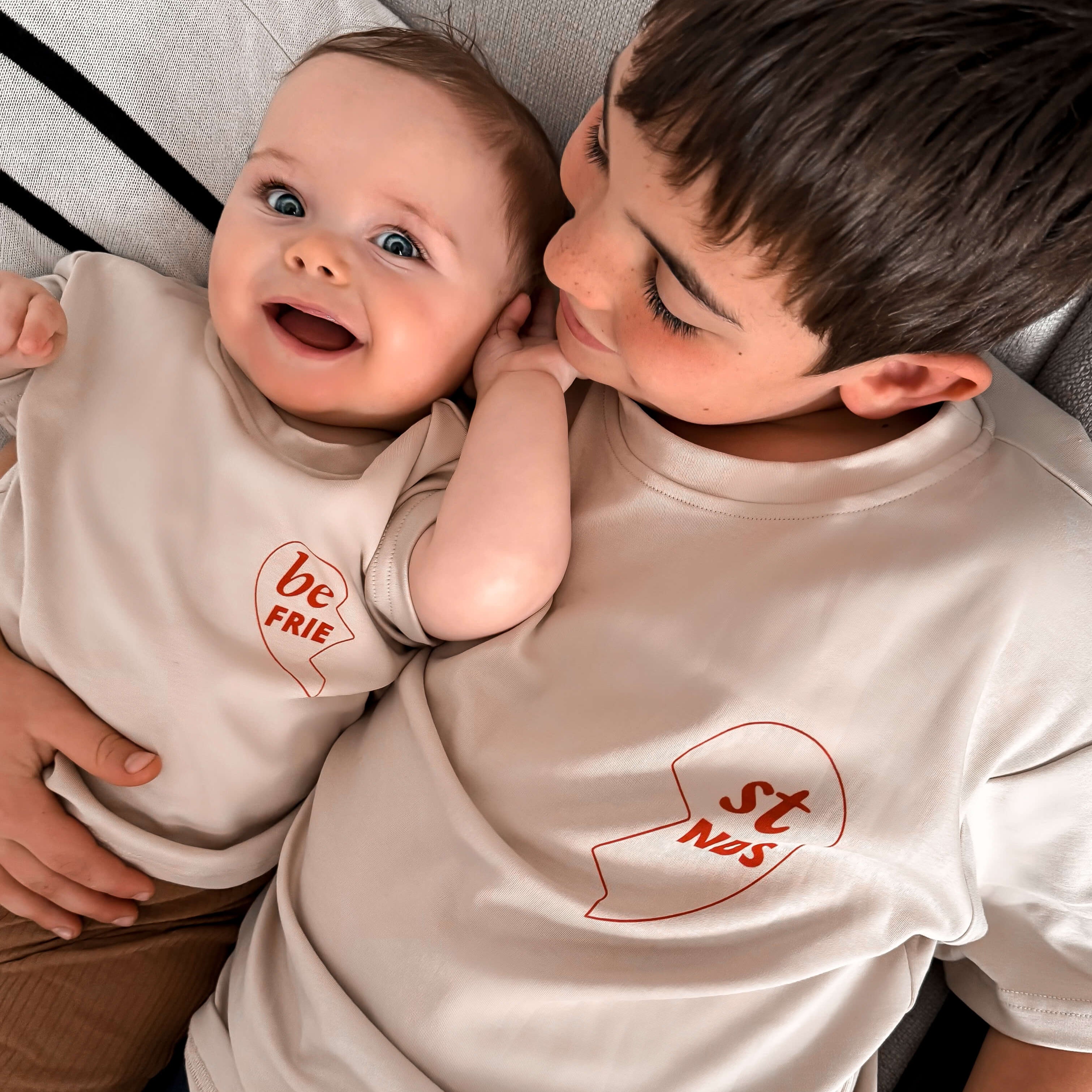 Two children wearing matching t-shirts with visible text, sitting close together.