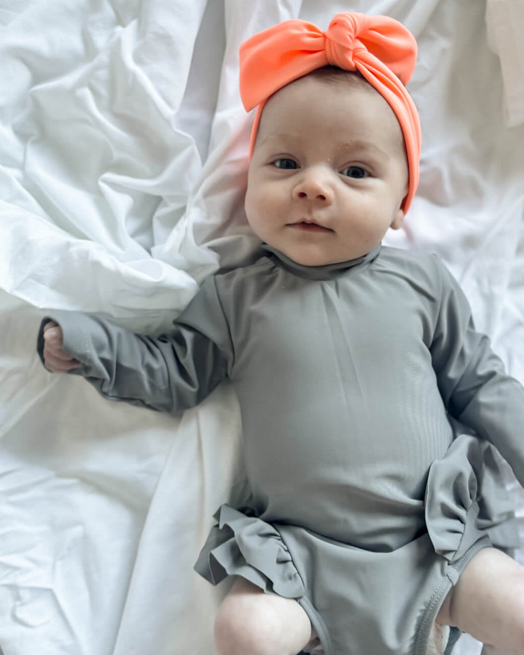 newborn baby girl swimsuit onesie with an orange headband lying on white bedding