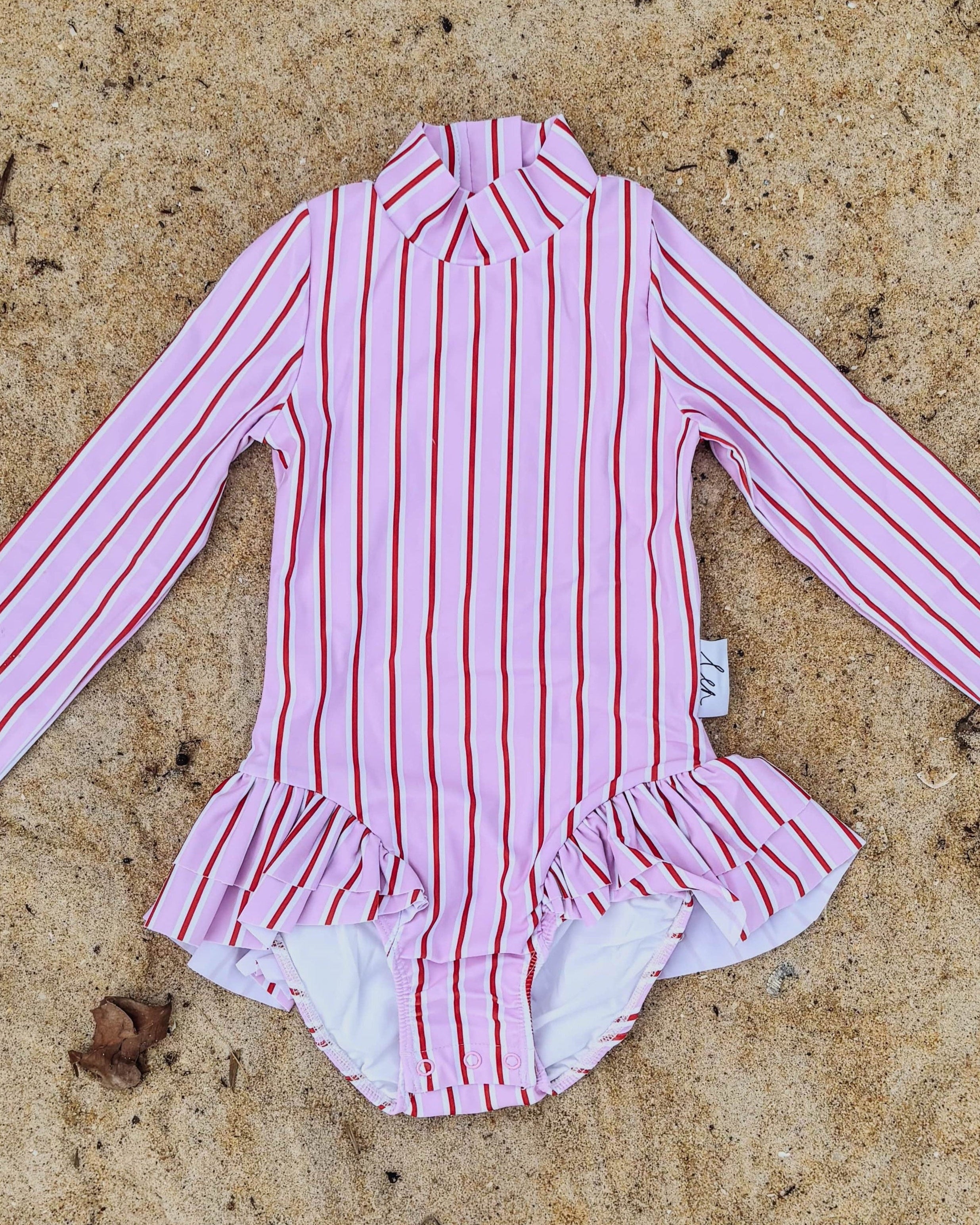Pink, red and white striped swimsuit on a sandy surface