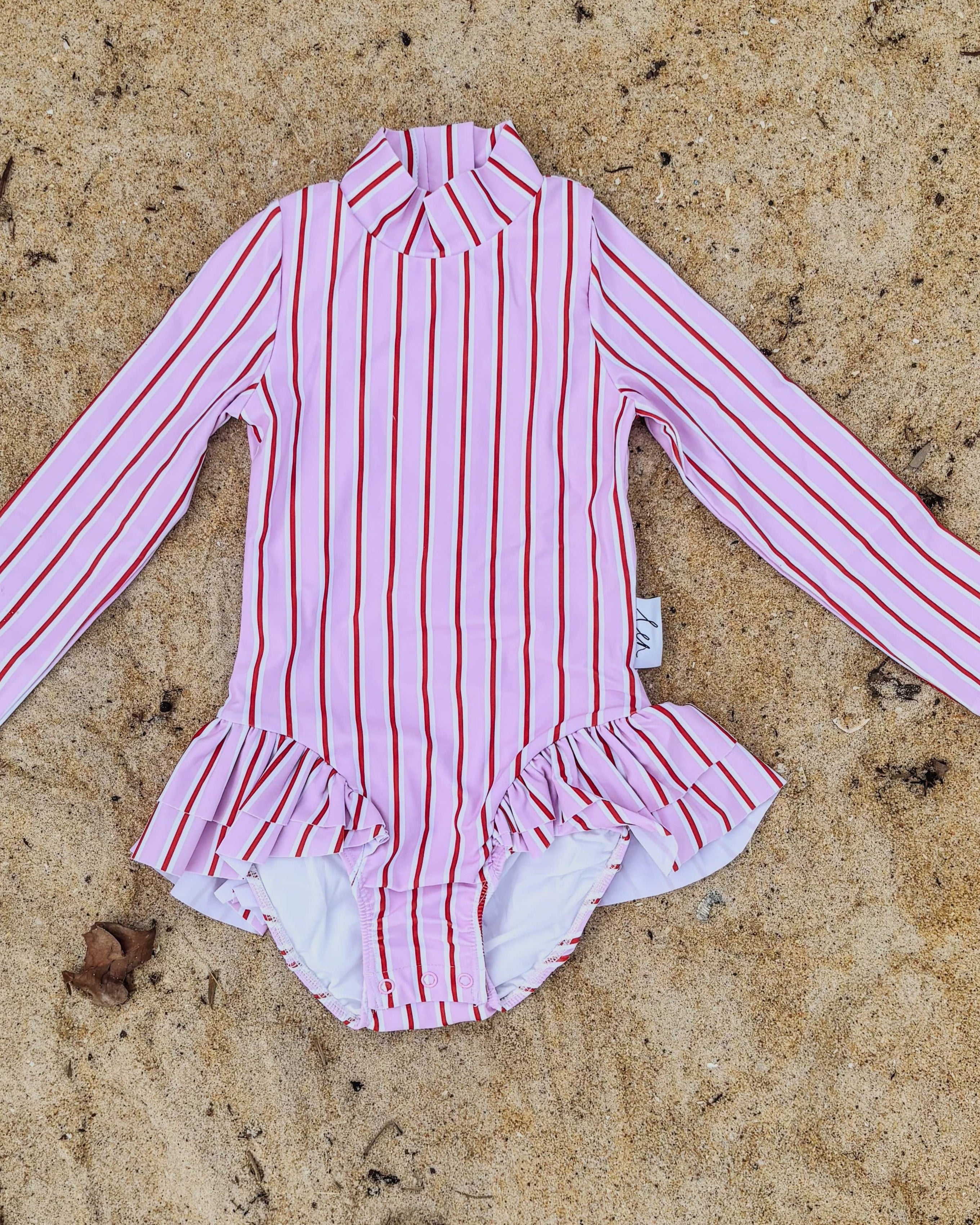 Pink, red and white striped swimsuit on a sandy surface