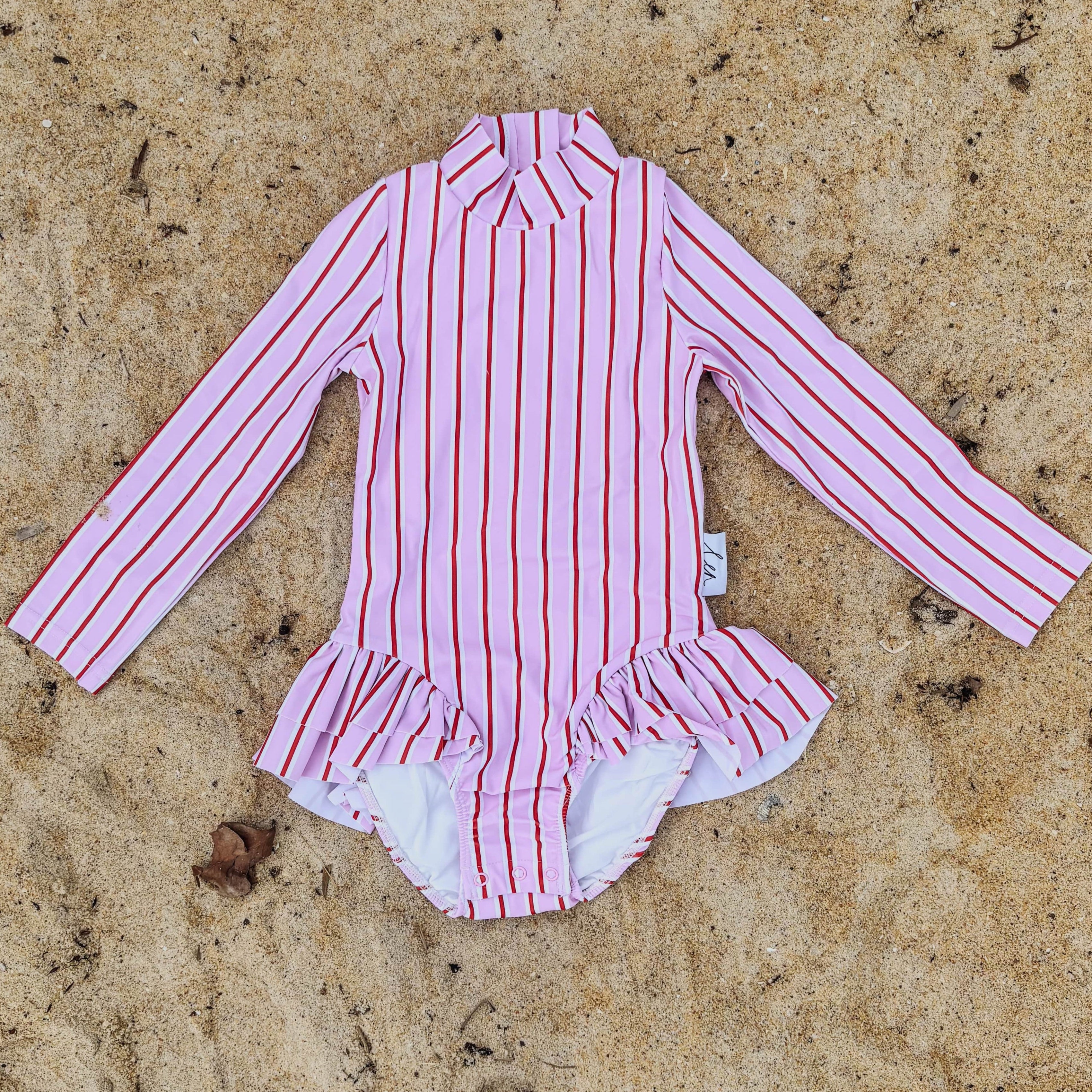 Pink, red and white striped swimsuit on a sandy surface