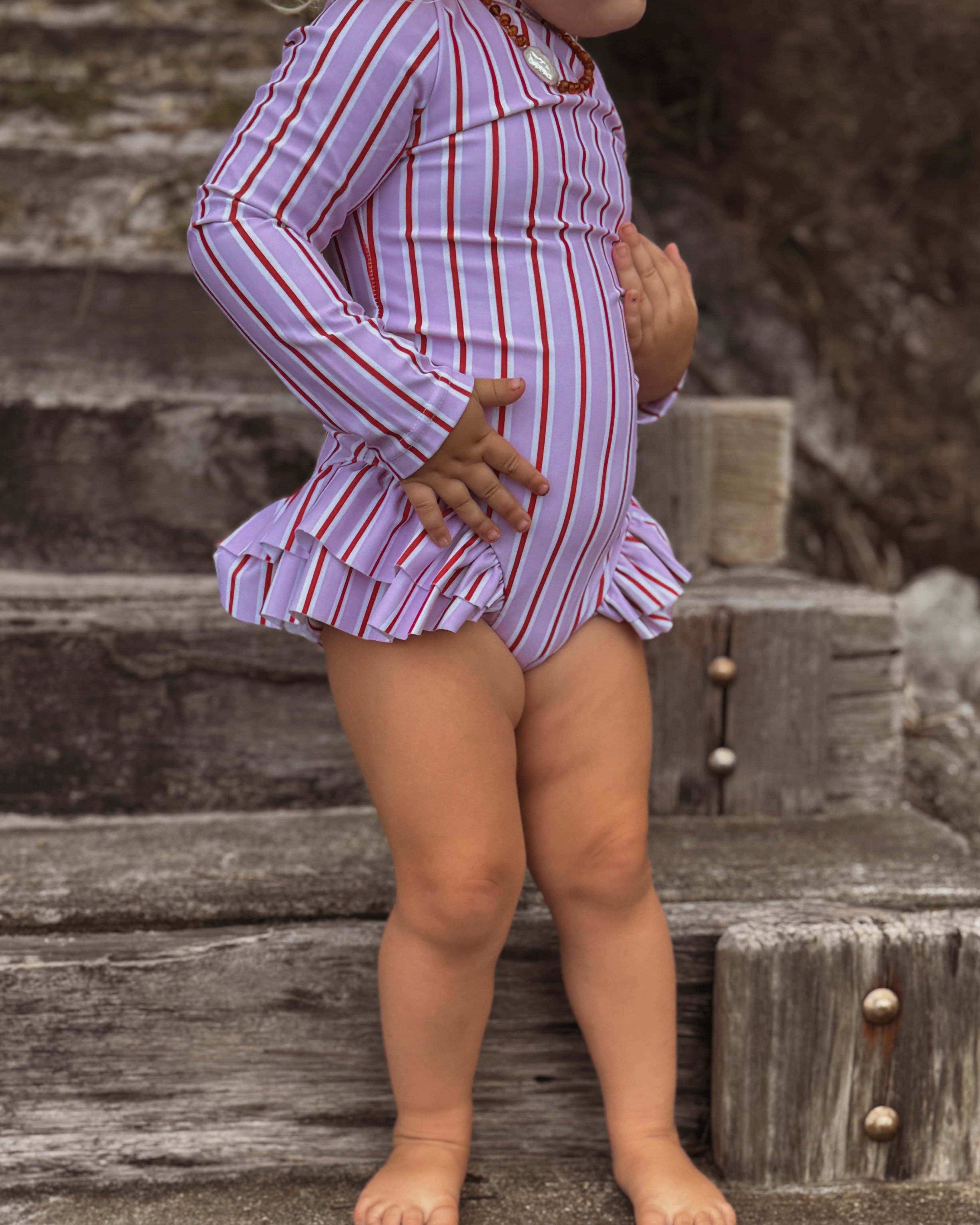 toddler girl in a pink and white striped nappy change swimsuit standing on wooden steps outdoors