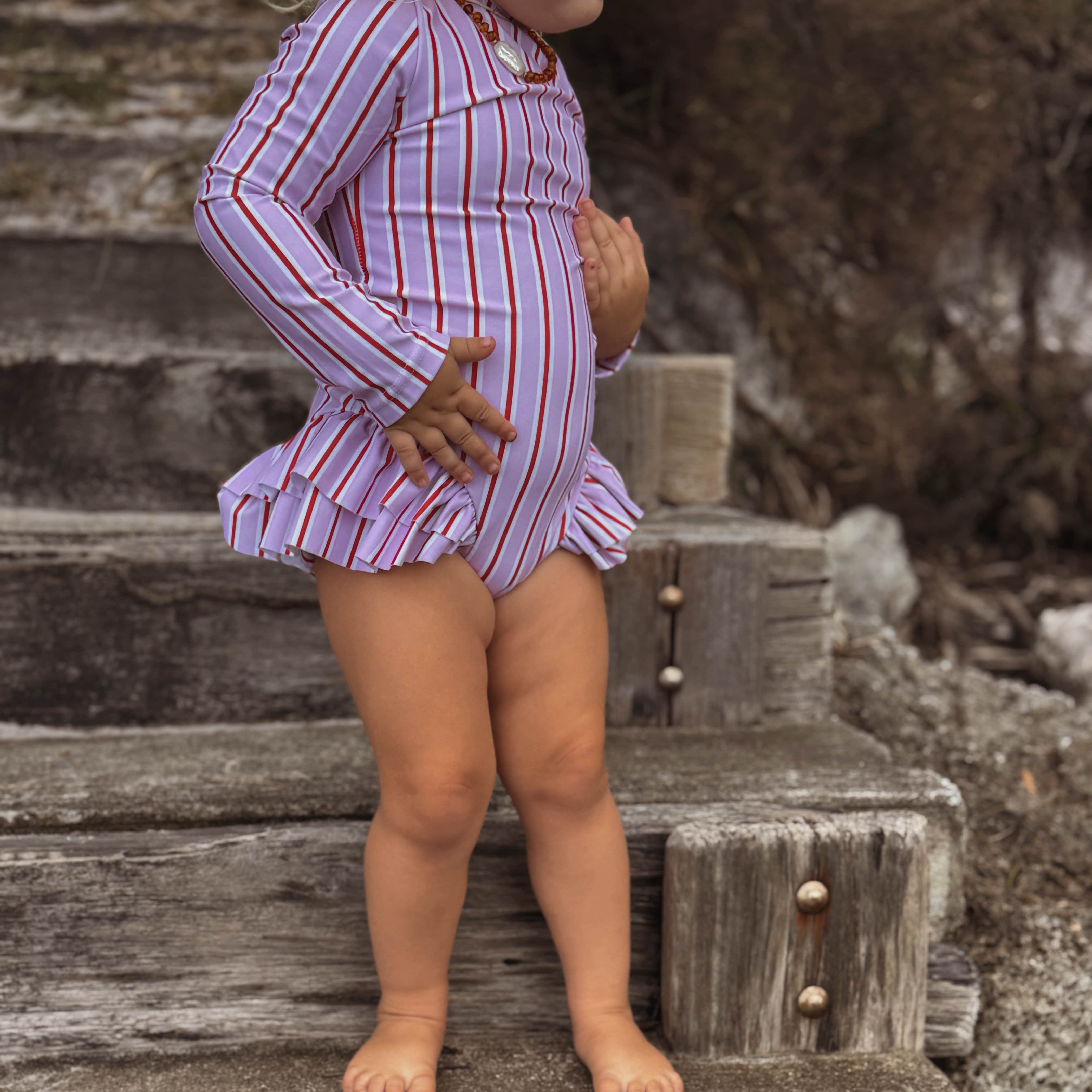 toddler girl in a pink and white striped nappy change swimsuit standing on wooden steps outdoors