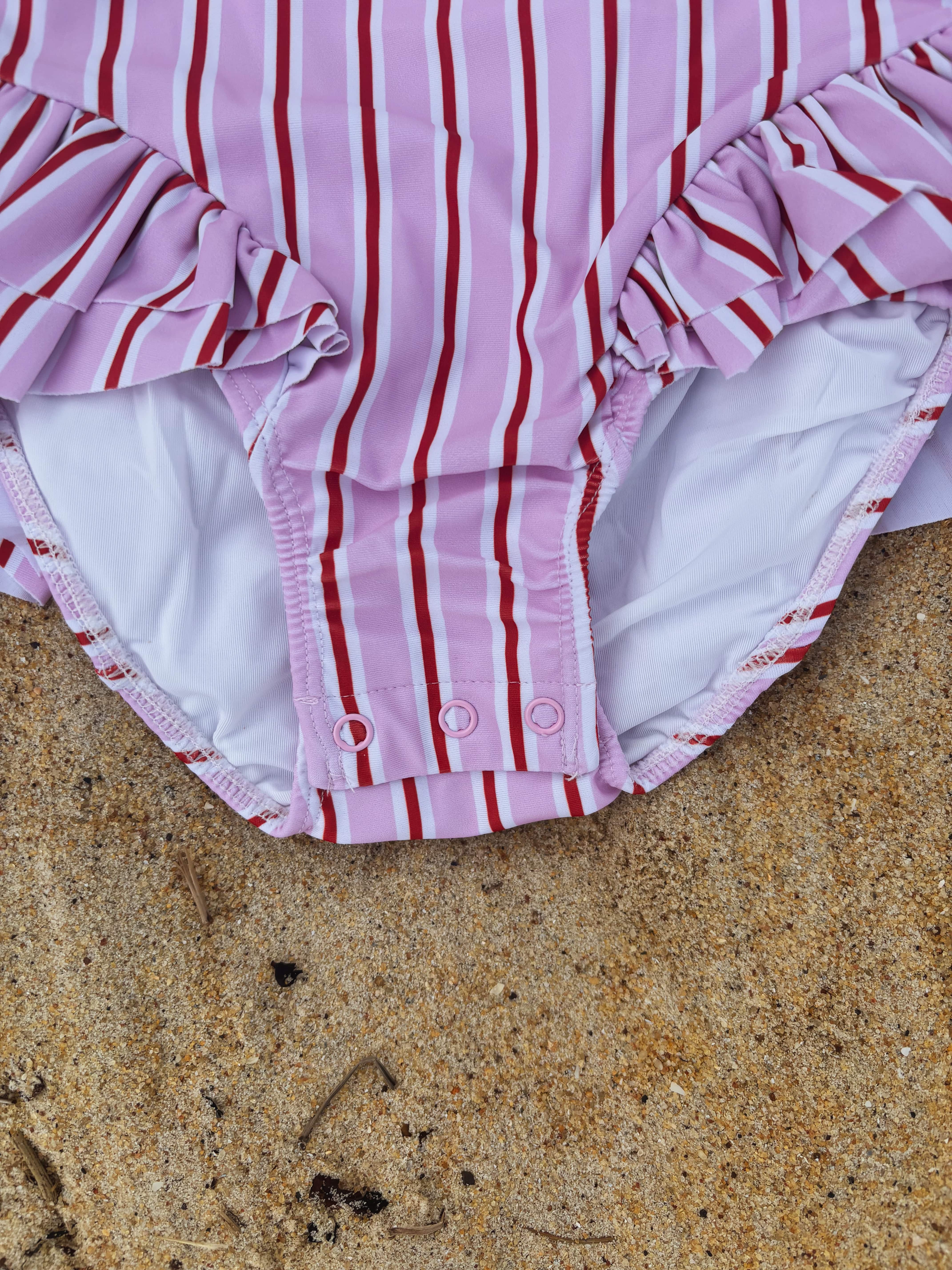 Pink and red striped baby diaper swimsuit with ruffles on a sandy surface