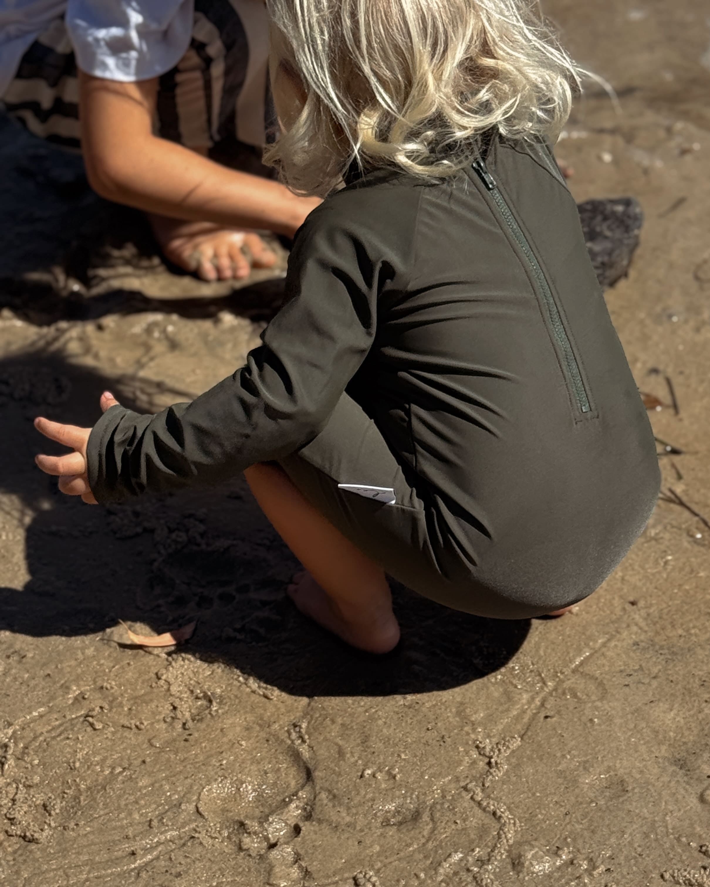 toddler wearing infant swimwear that is an all in one rash suit that olive and has nappy change snaps and large rear zip