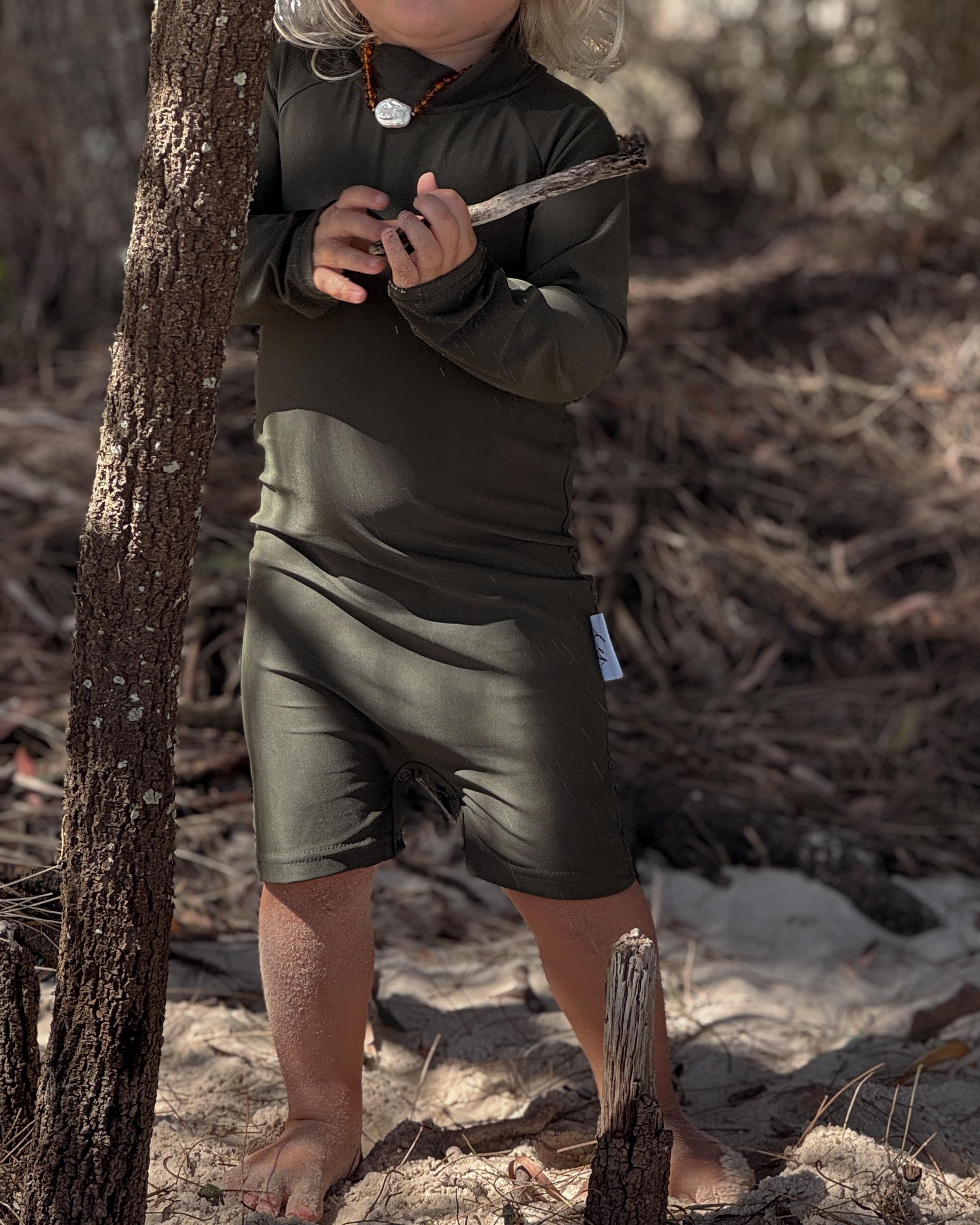 toddler wearing infant swimwear that's an all in one rashsuit that olive and has nappy change snaps