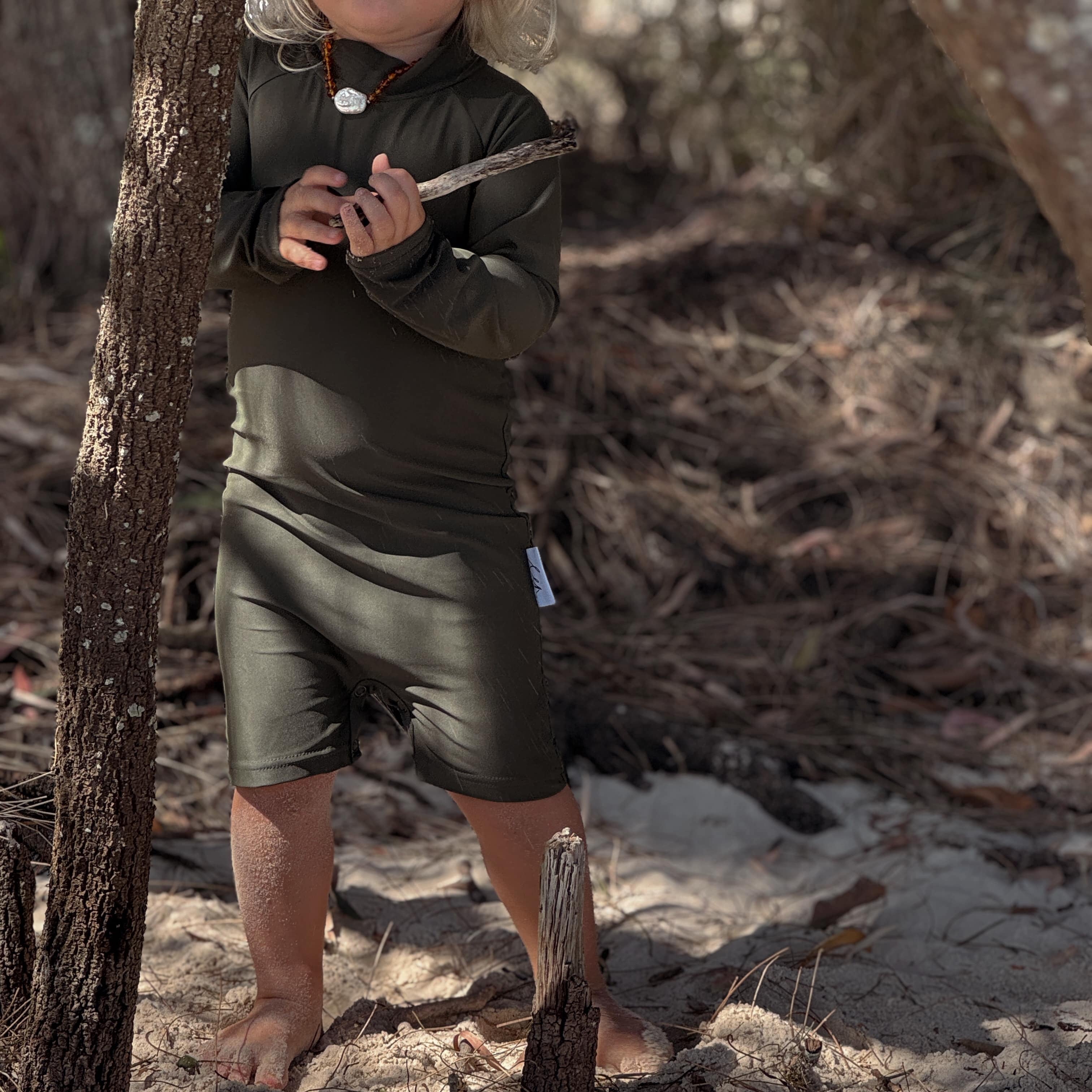 toddler wearing an all in one rashsuit that olive and has nappy change snaps