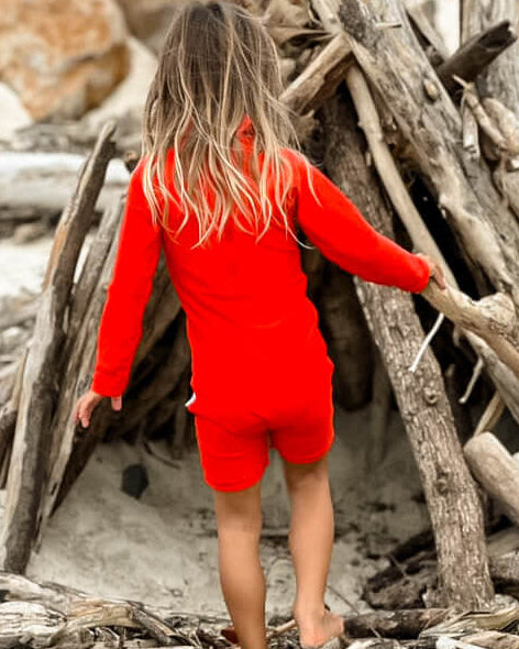 young child playing at beach in a bright neon red one piece rashie