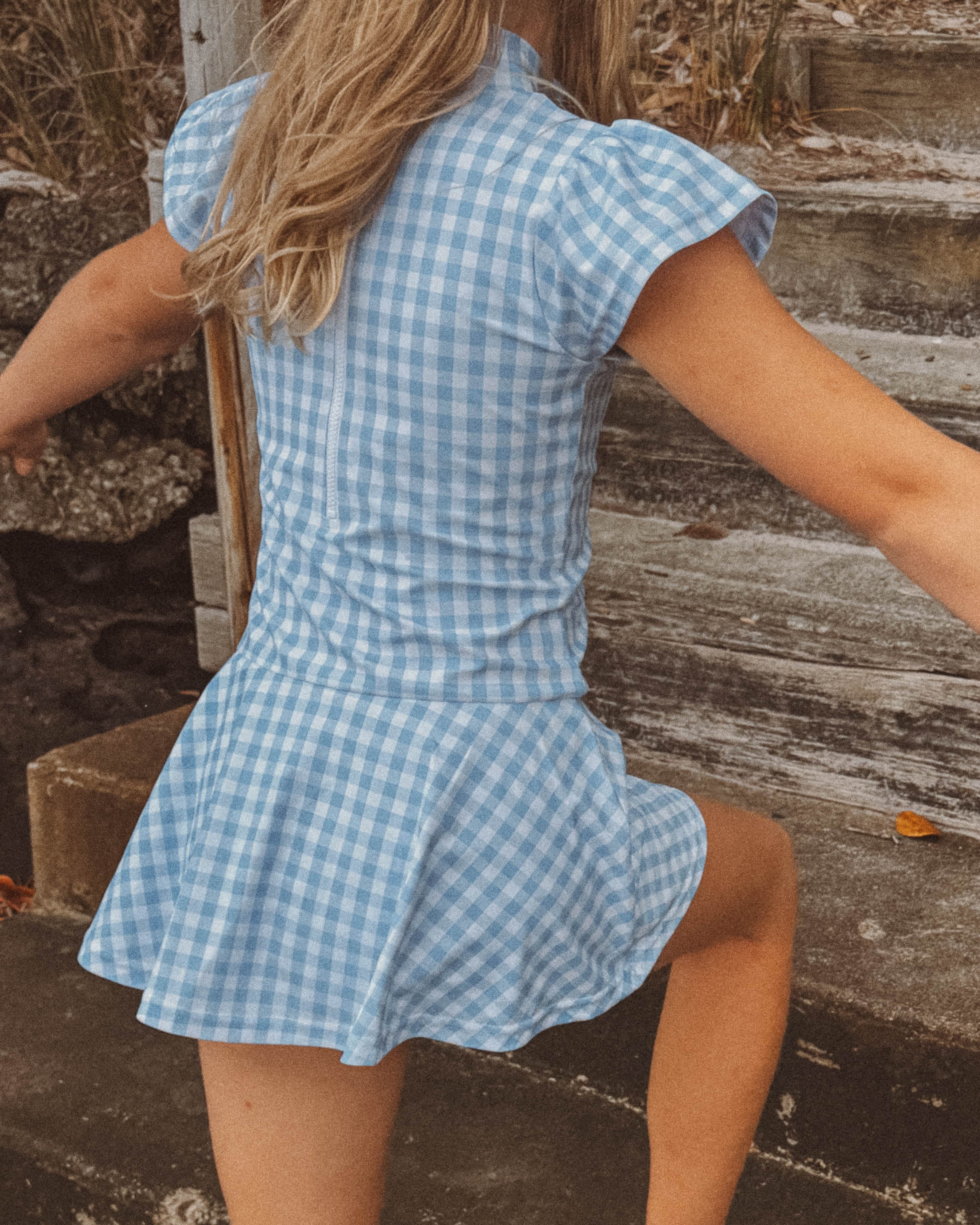 young girl in a blue checkered swim dress standing on stone steps.