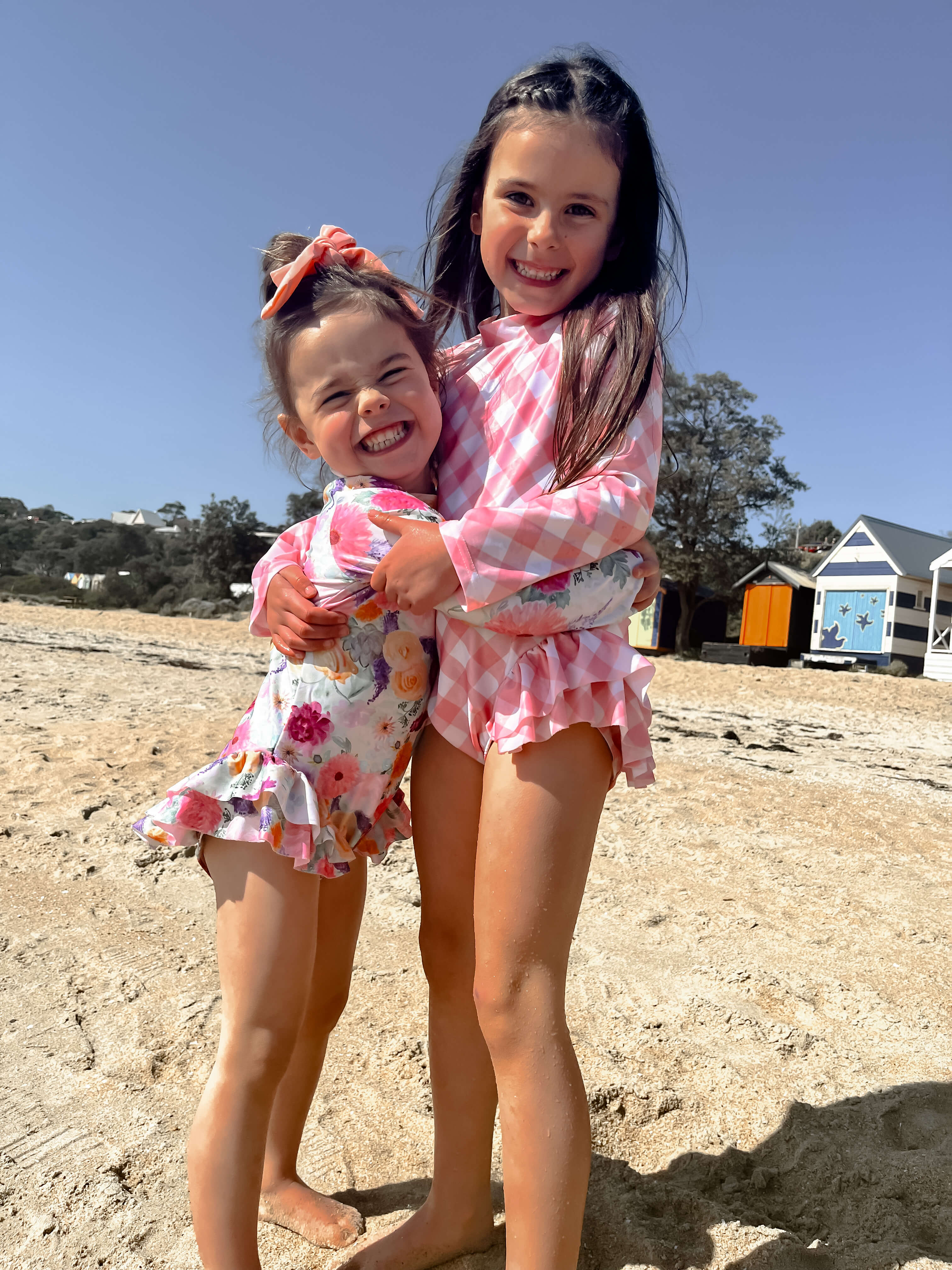 two girls at the beach wearing long sleeved bright colored premium swimsuits with change snaps 