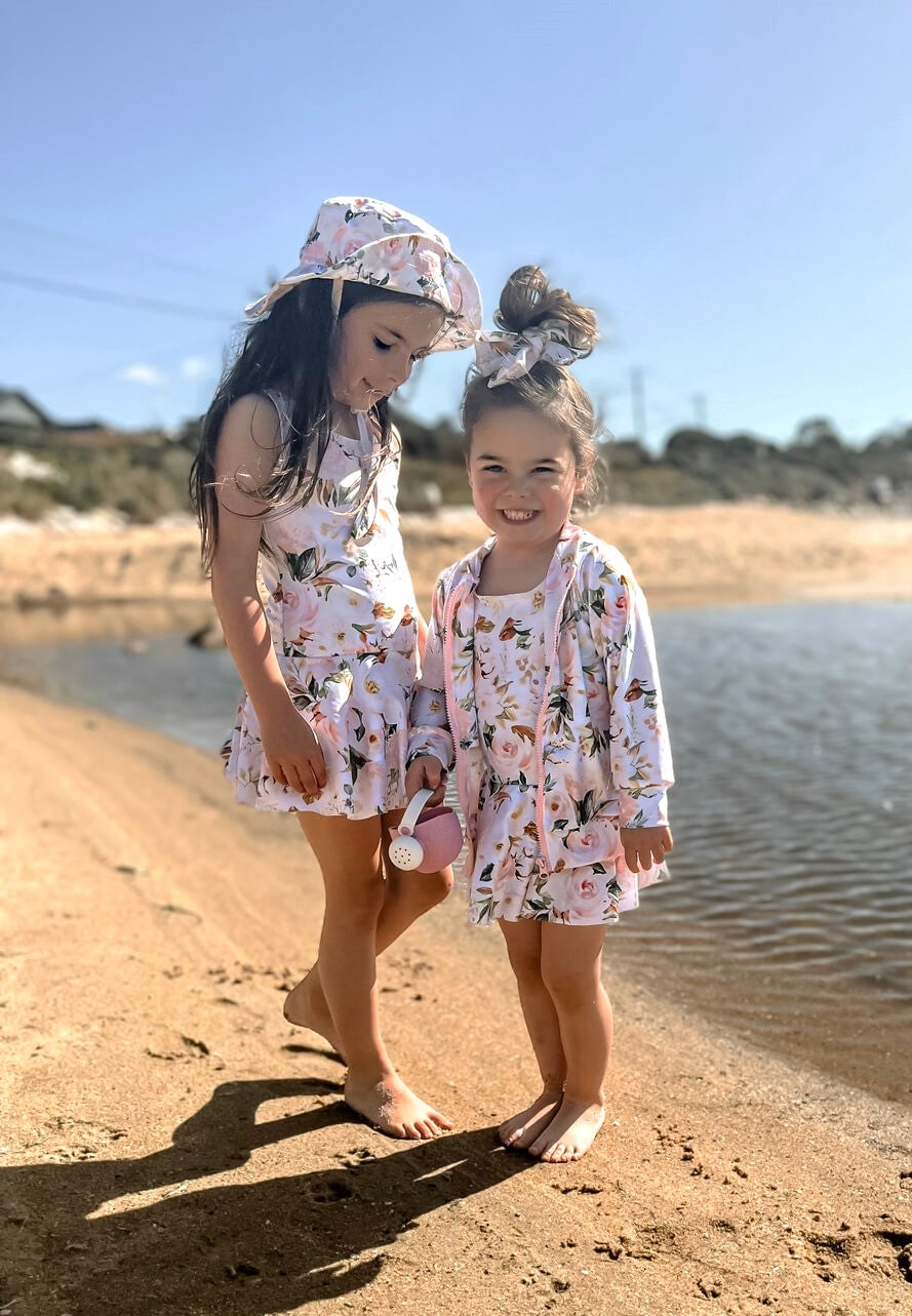 two girls at the beach in matching snap change swimsuits with matching jackets, hats and accessories