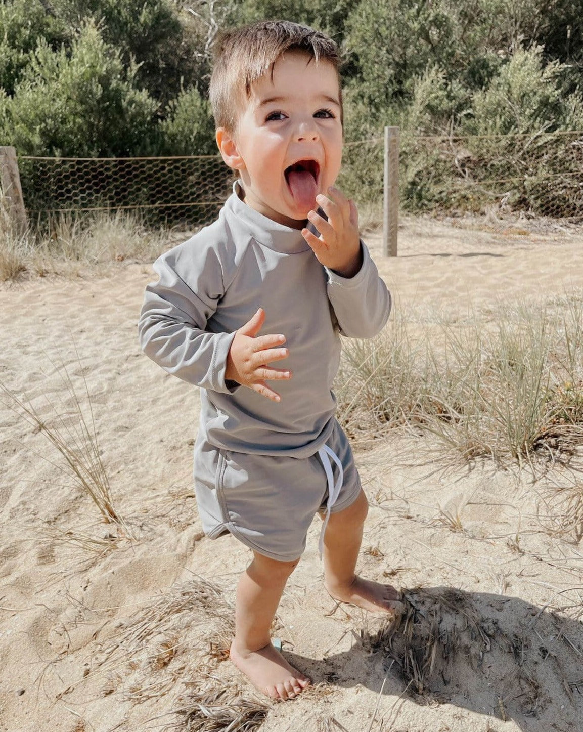 toddler on the beach playing in a grey two piece swim set with large rear zip