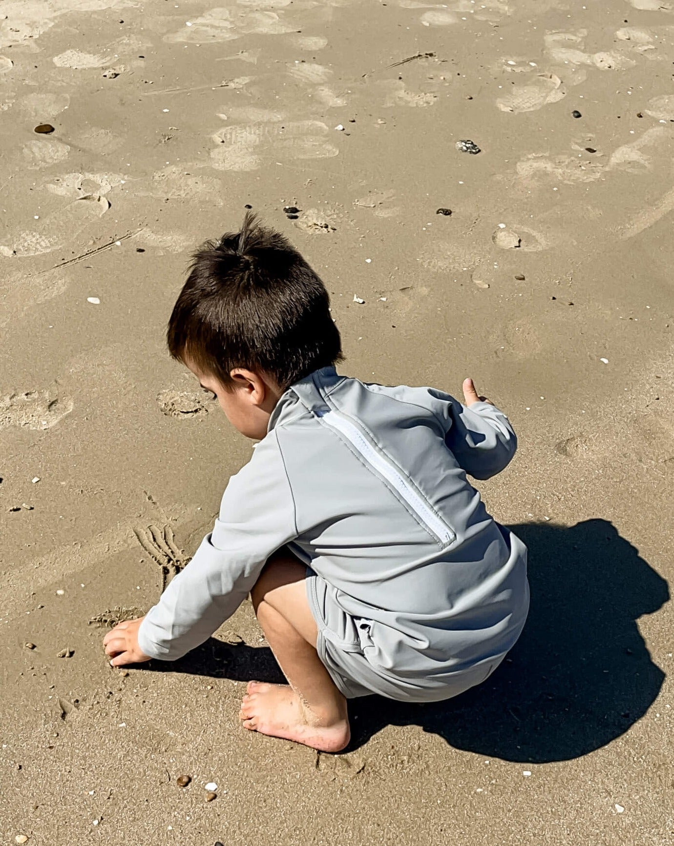 young boy playing on the beach with his back to the camera wearing a long sleeve grey matching rash set