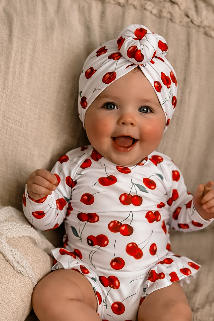 Baby wearing a cherry-patterned outfit and headband on a beige background
