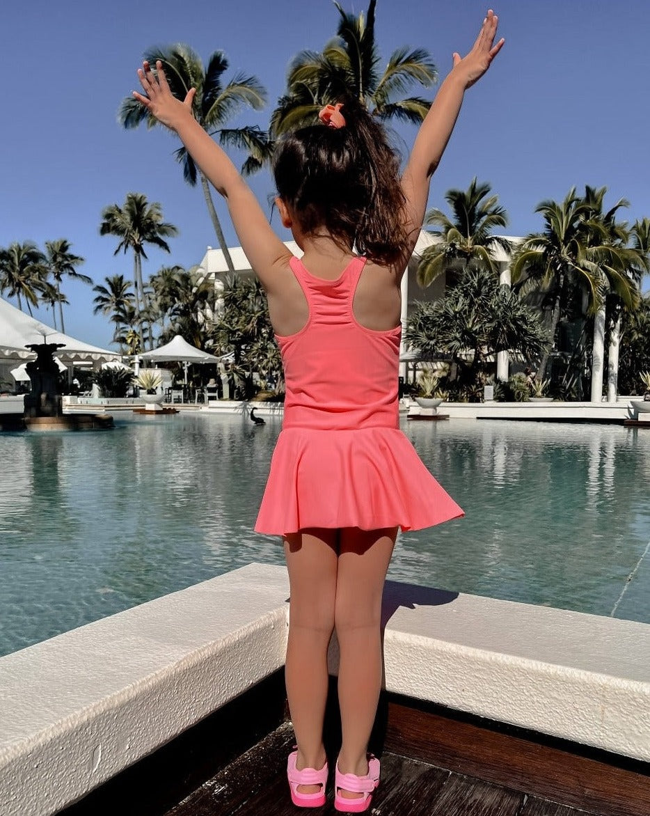 Girl in swim dress with snap closures facing a pool  and matching hair tie