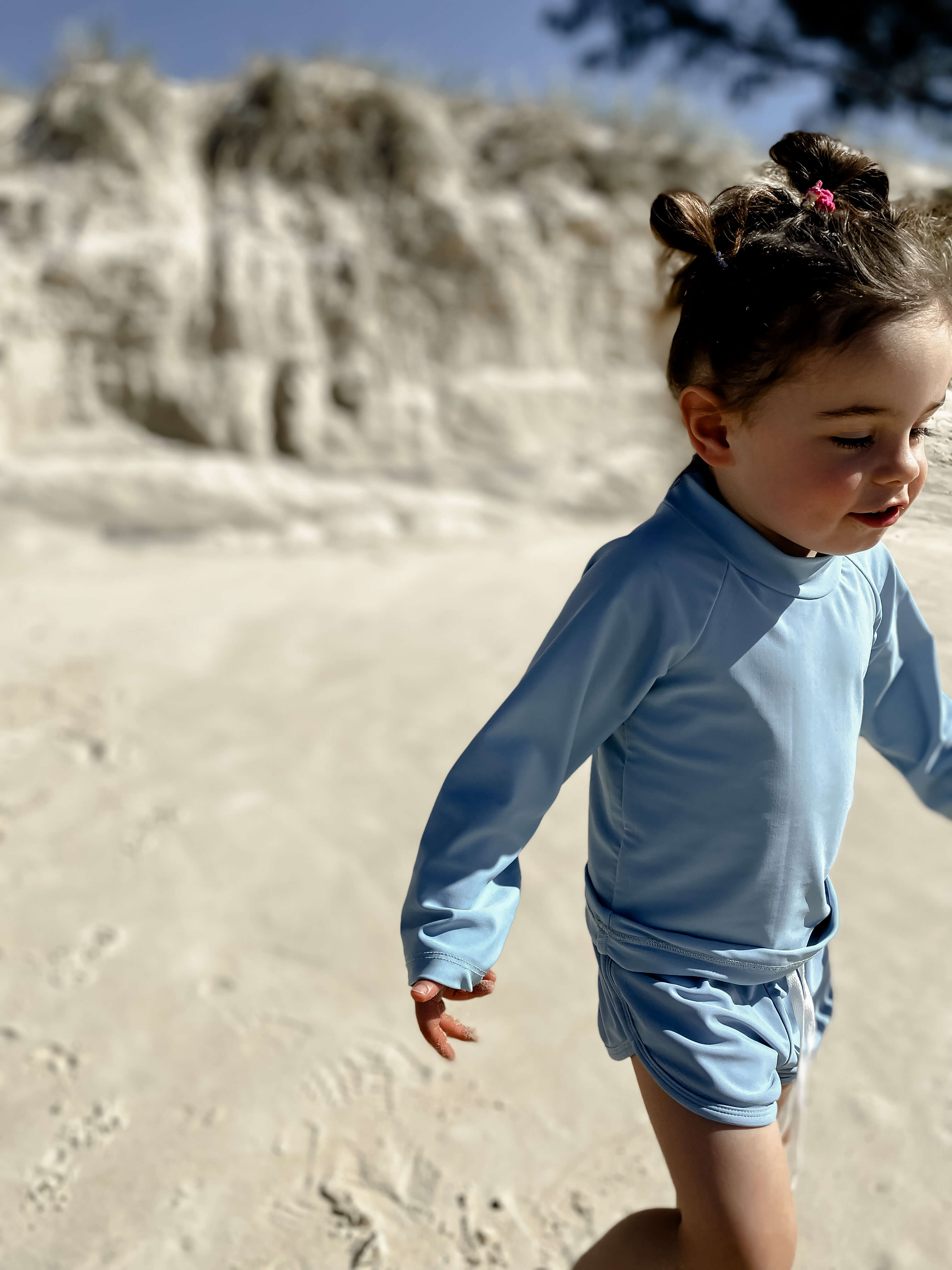 A child wearing a bright blue two peice rash top and swim short at the beach