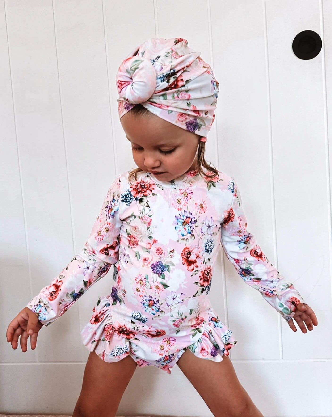 toddler girl in a matching swim turban and long sleeve swimsuit with snaps at the bottom