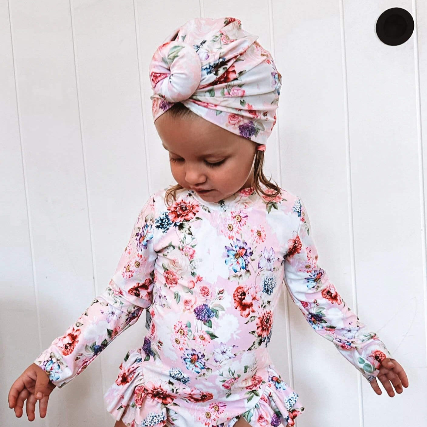 toddler girl in a matching swim turban and long sleeve swimsuit with snaps at the bottom