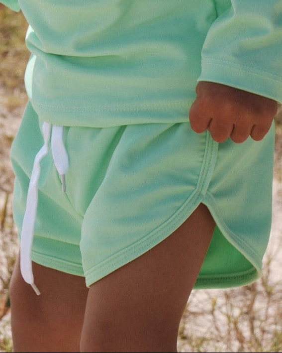 Child wearing a bright light green swim short outfit and cap outdoors