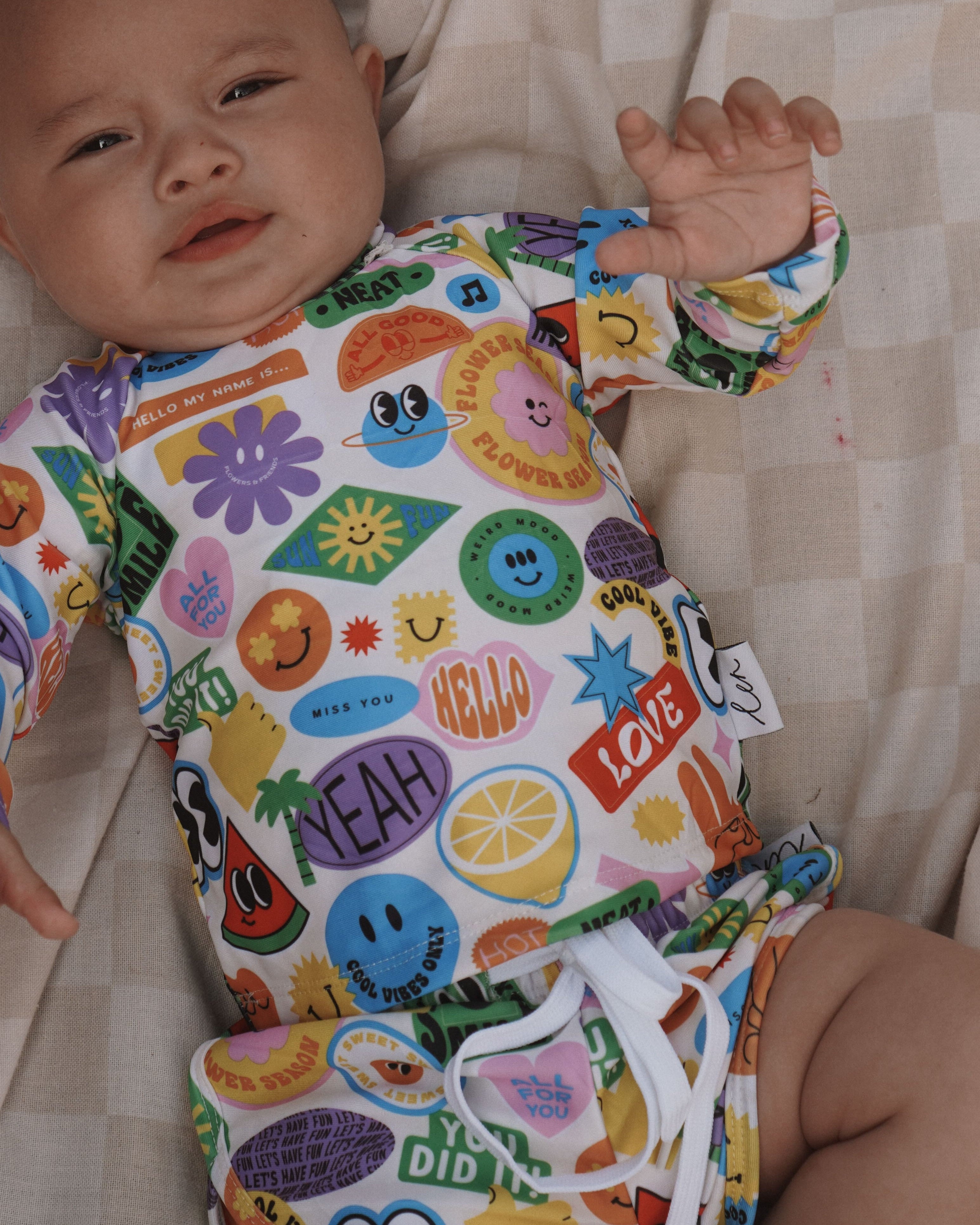 Baby wearing a colorful bright newborn swimsuit outfit with cartoon designs on a checkered blanket