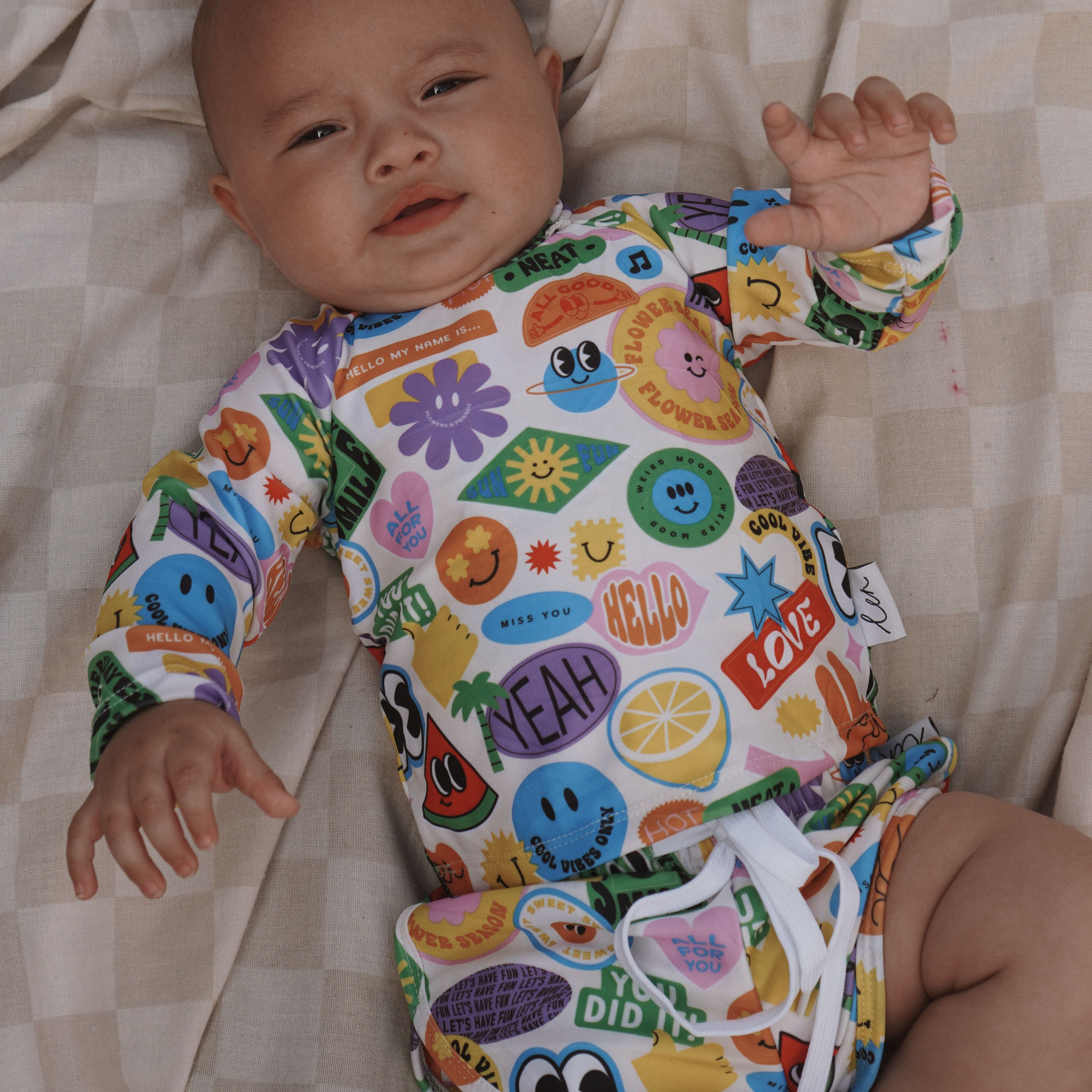 Baby wearing a colorful bright newborn swimsuit outfit with cartoon designs on a checkered blanket