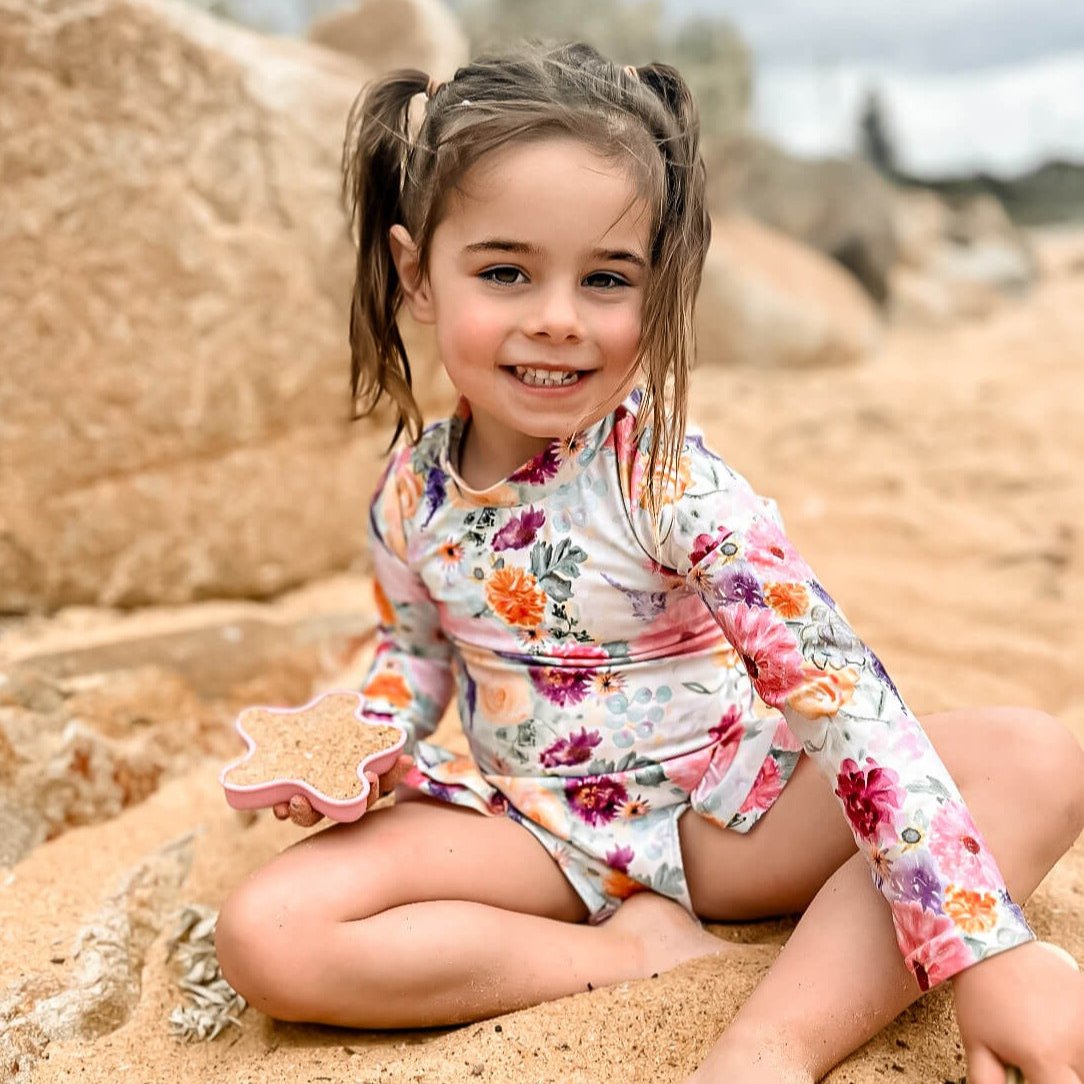 Young girl wearing a nappy change swimsuit with snaps in a bright floral pattern