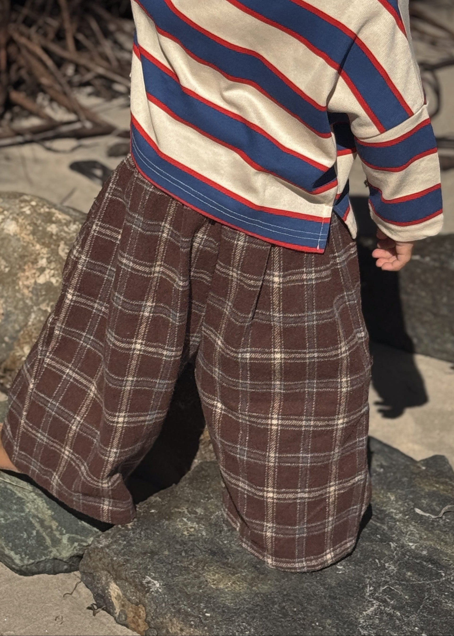 Child wearing a striped sweater and plaid pants standing on a stone surface.