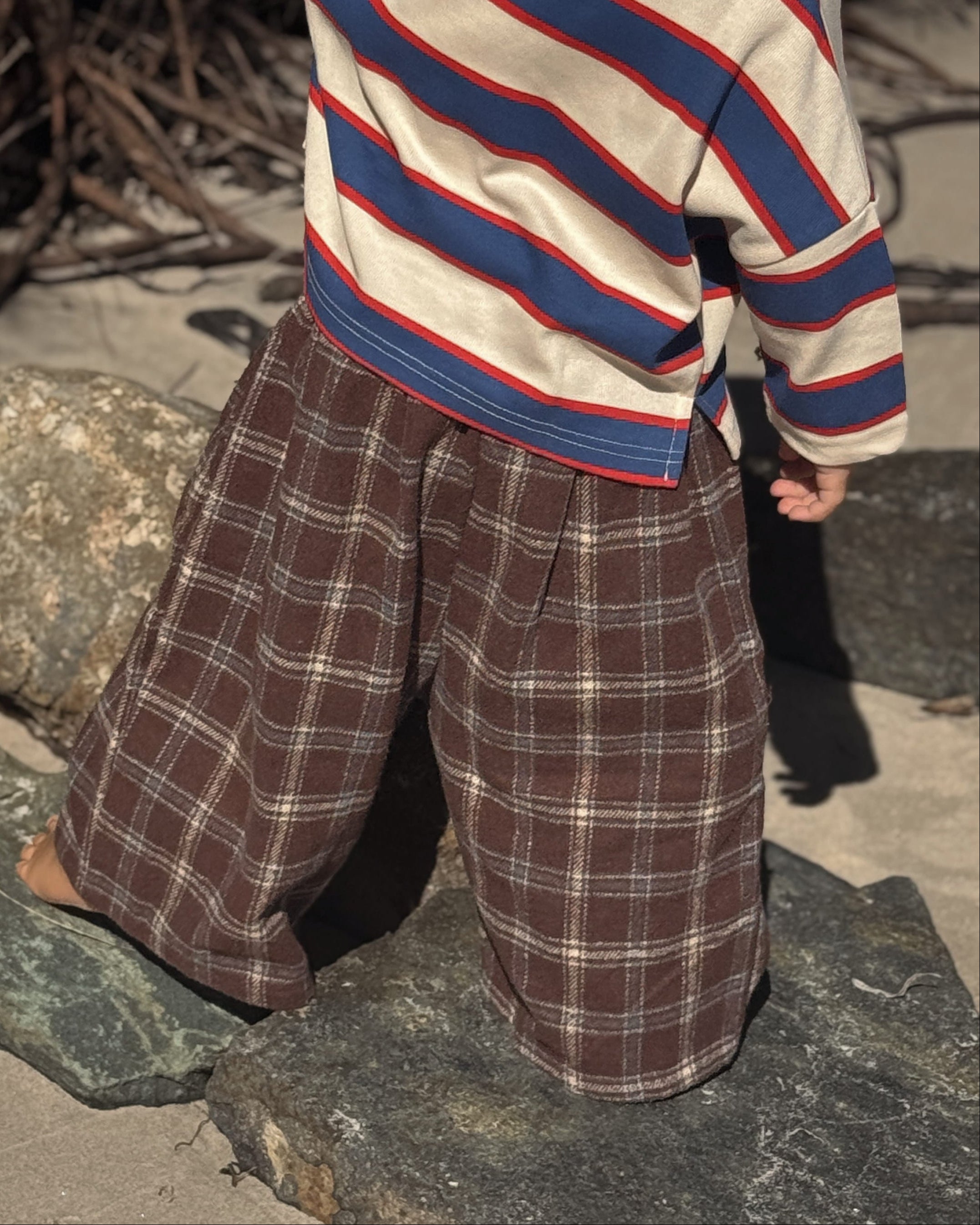 Child wearing a striped sweater and plaid pants standing on a stone surface.