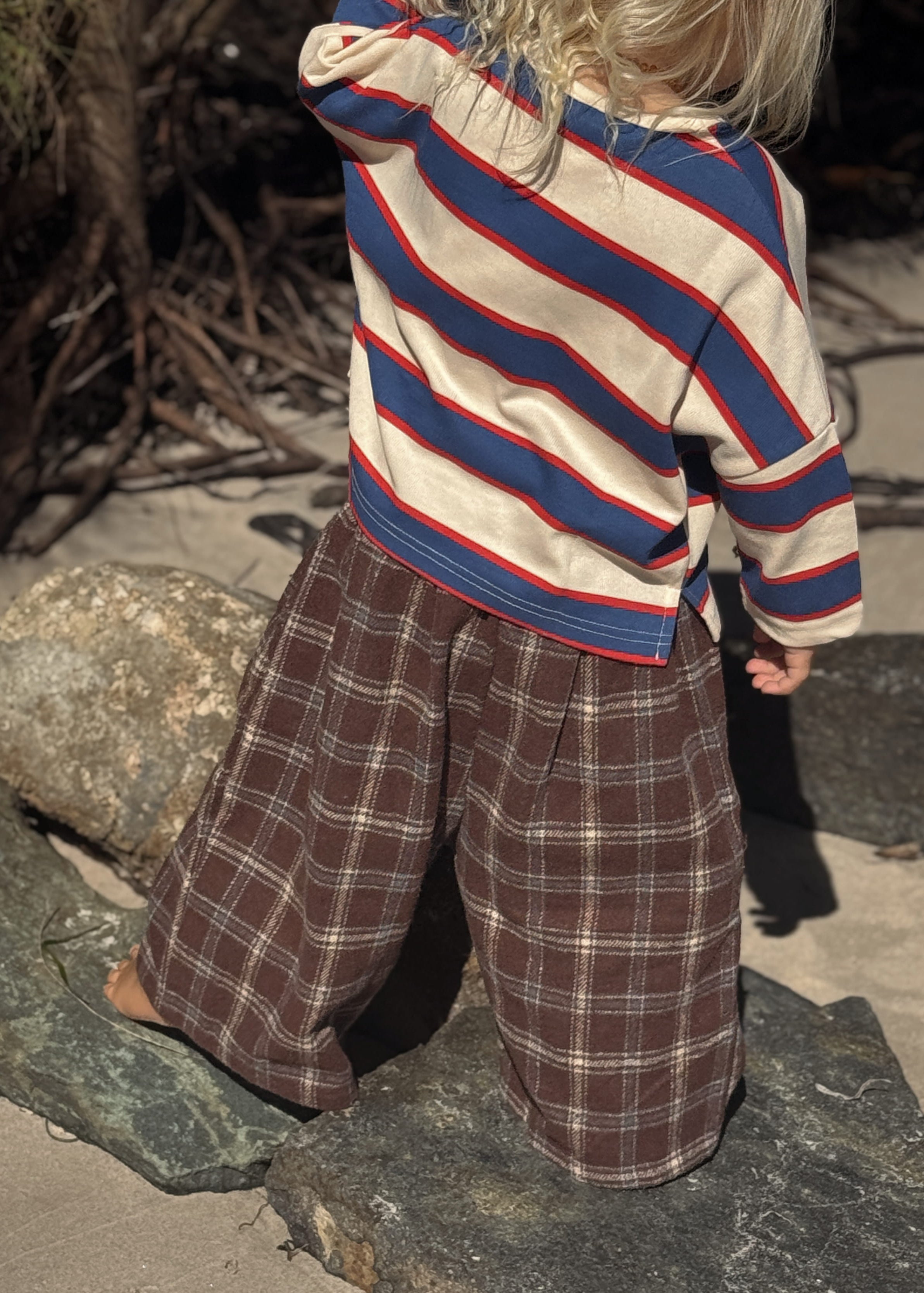 Child wearing a striped sweater and plaid pants standing on a stone surface.