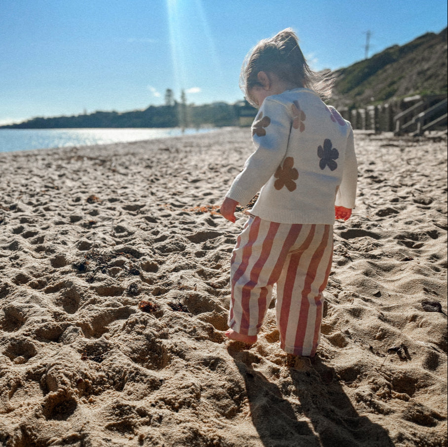 Child playing on a sandy beach with ocean and clear sky in the background