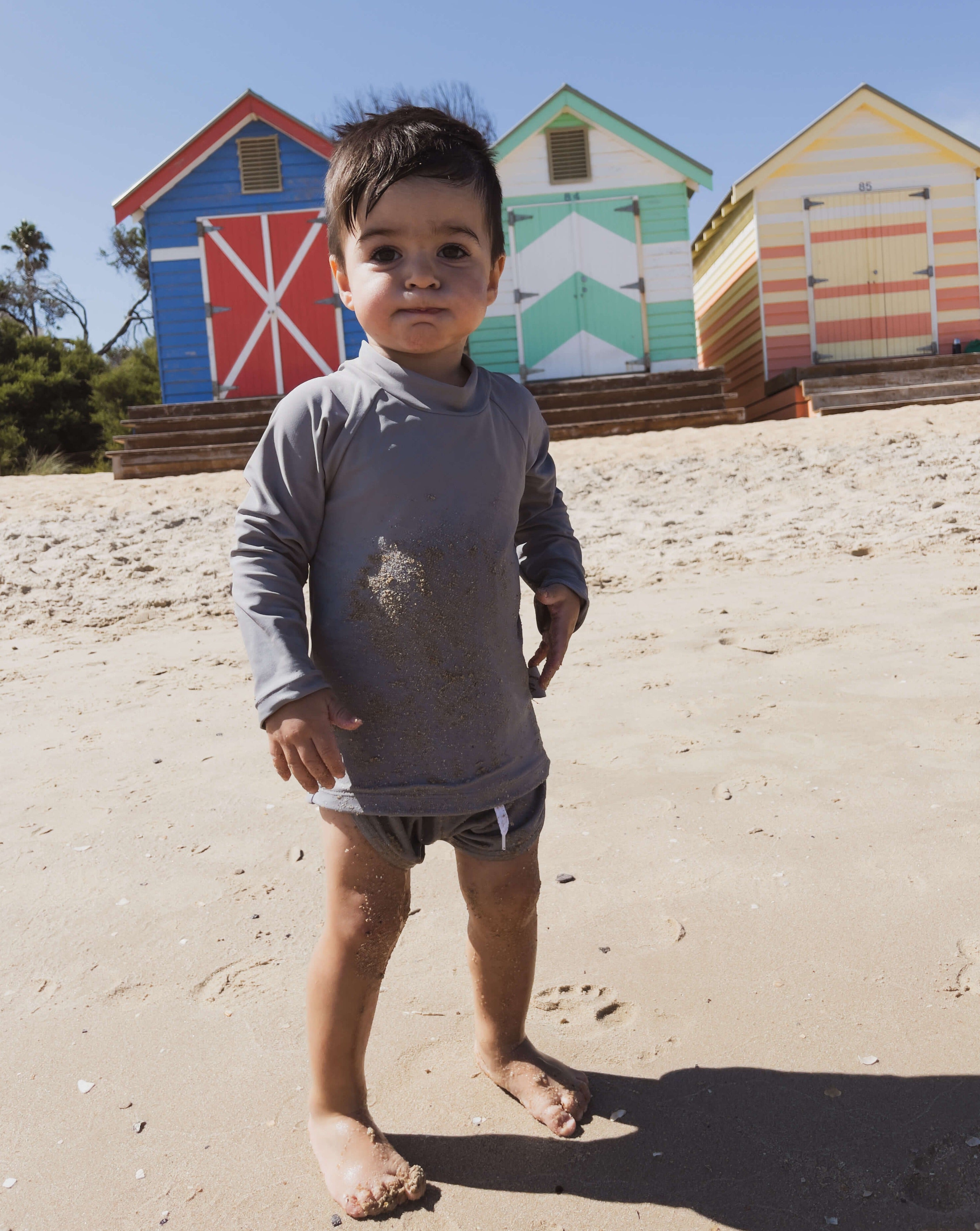 toddler boy playing on the beach wearing a grey rash swim top and matching shorts with a large zip at the back