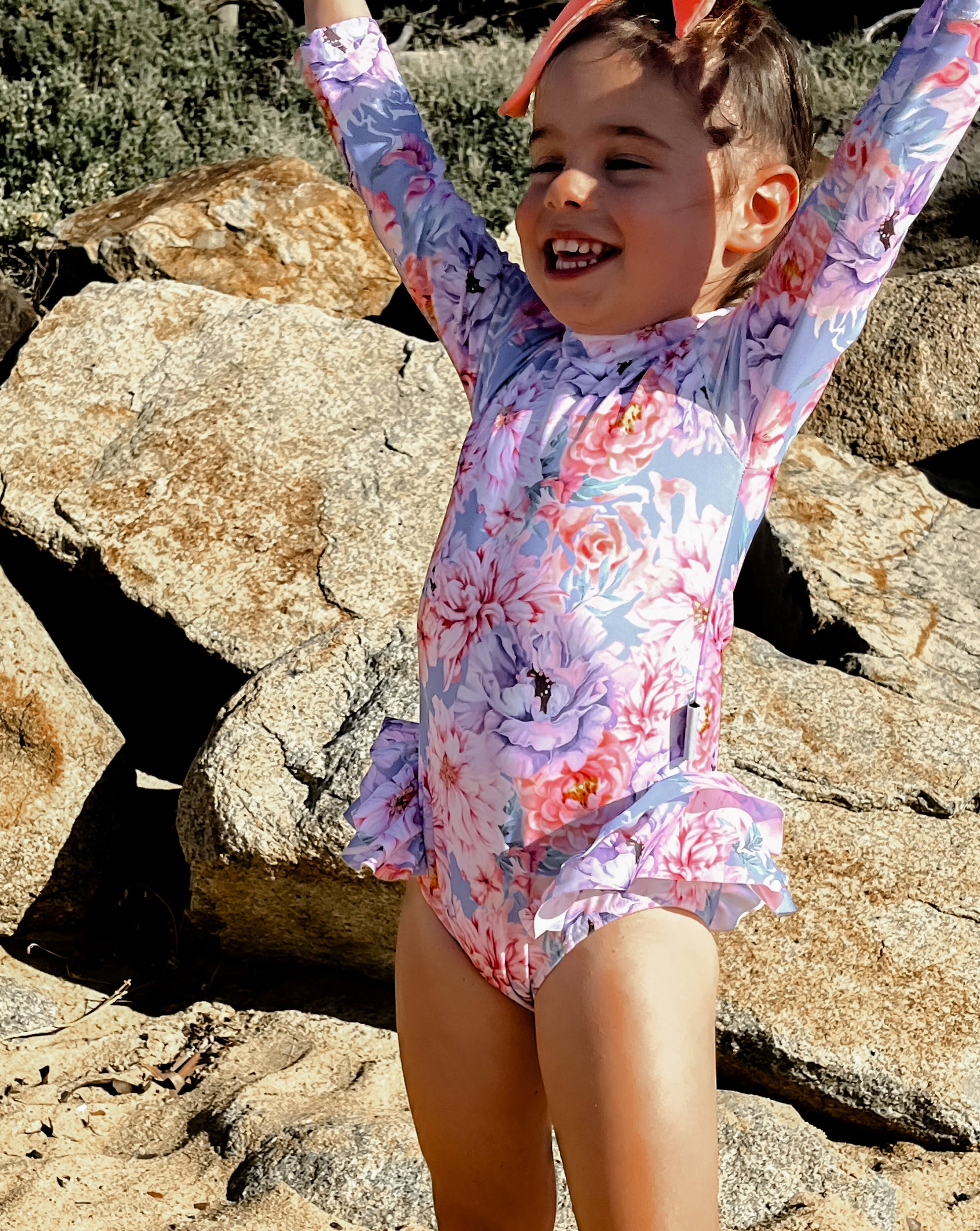Toddler girl playing at the beach in the best long sleeve kids swimsuit with flowers and nappy change snaps